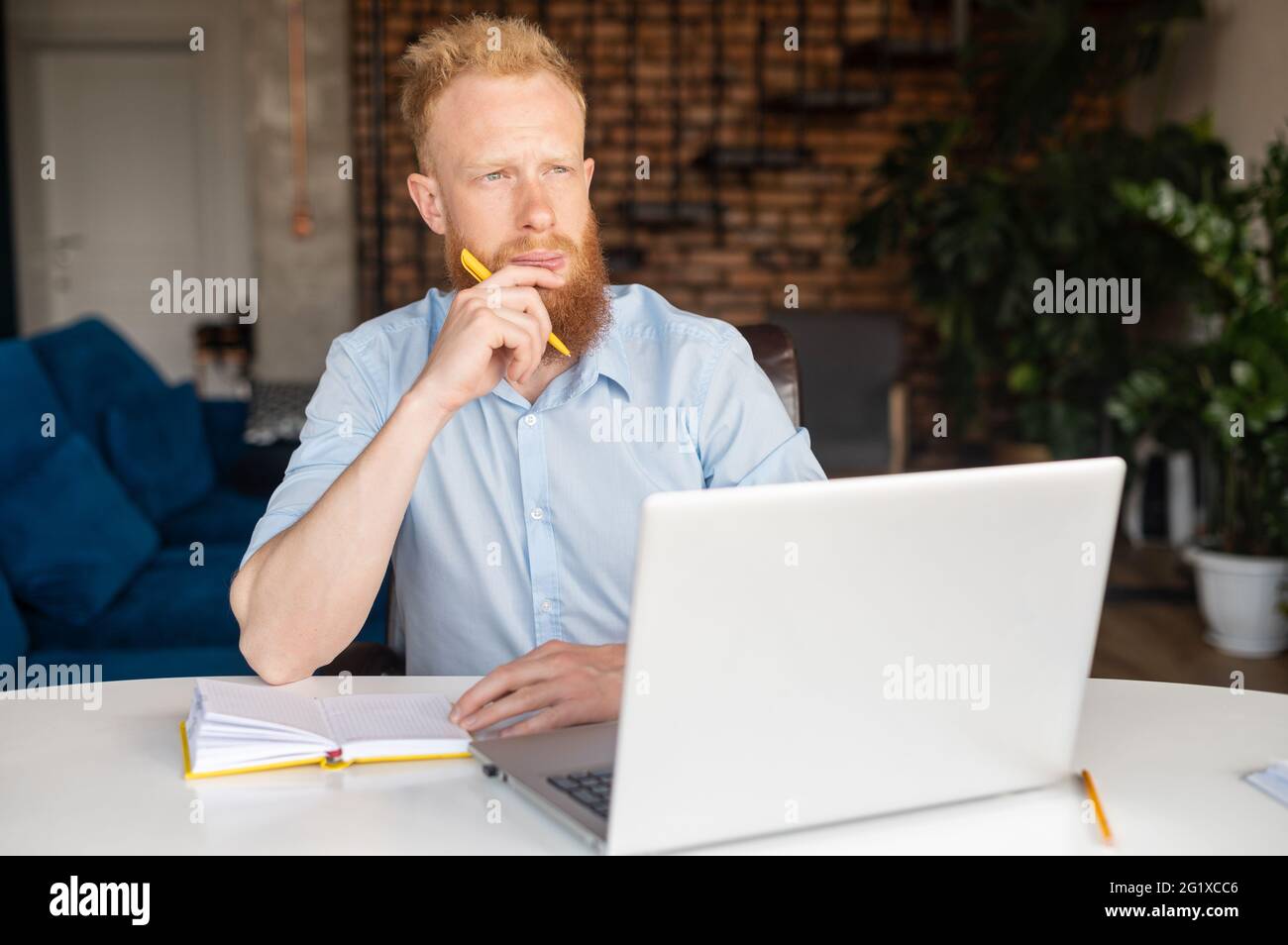 Nachdenklicher, moderner rothaariger Geschäftsmann, der nach neuen Ideen sucht, mit einem Laptop im Heimbüro am Schreibtisch sitzt, in Gedanken verloren schaut, Aufgaben löst, plant Stockfoto