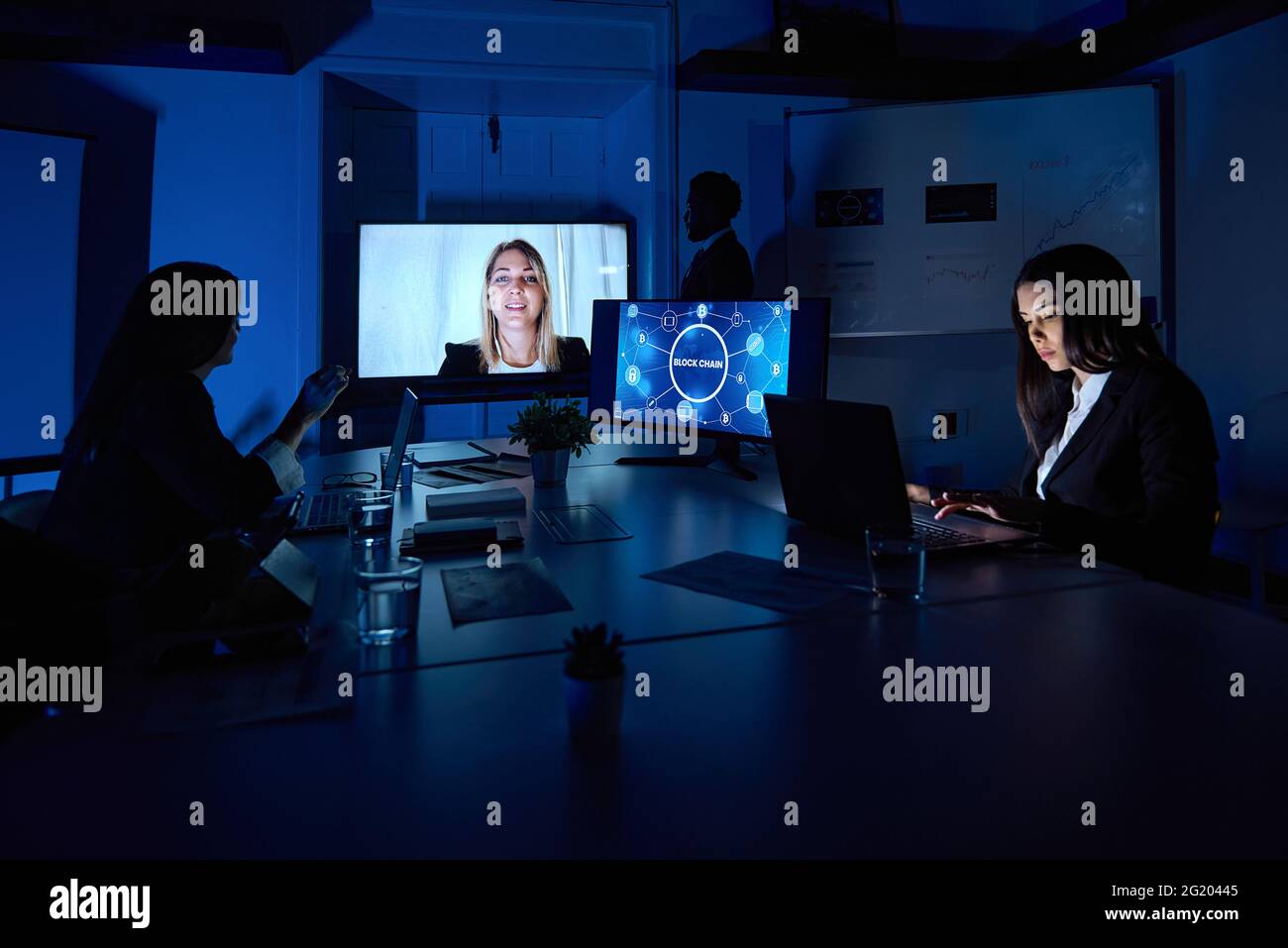 Kollegen, die während einer Online-Konferenz im dunklen Büro an Laptops arbeiten Stockfoto