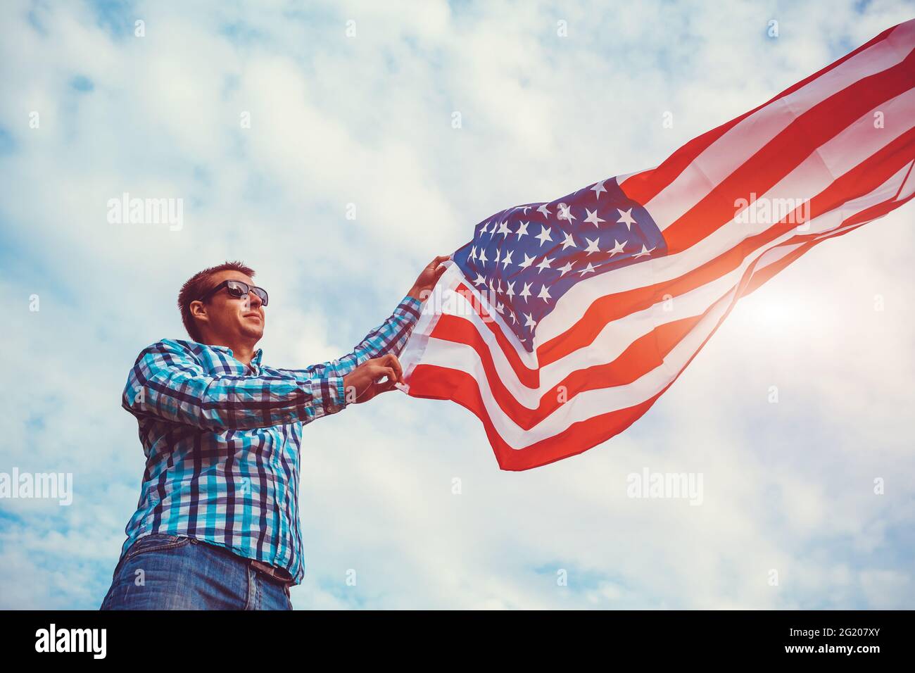 Mann, der die US-Flagge gegen den wolkigen Himmel hält. Feiern des Unabhängigkeitstages von Amerika. Juli Stockfoto