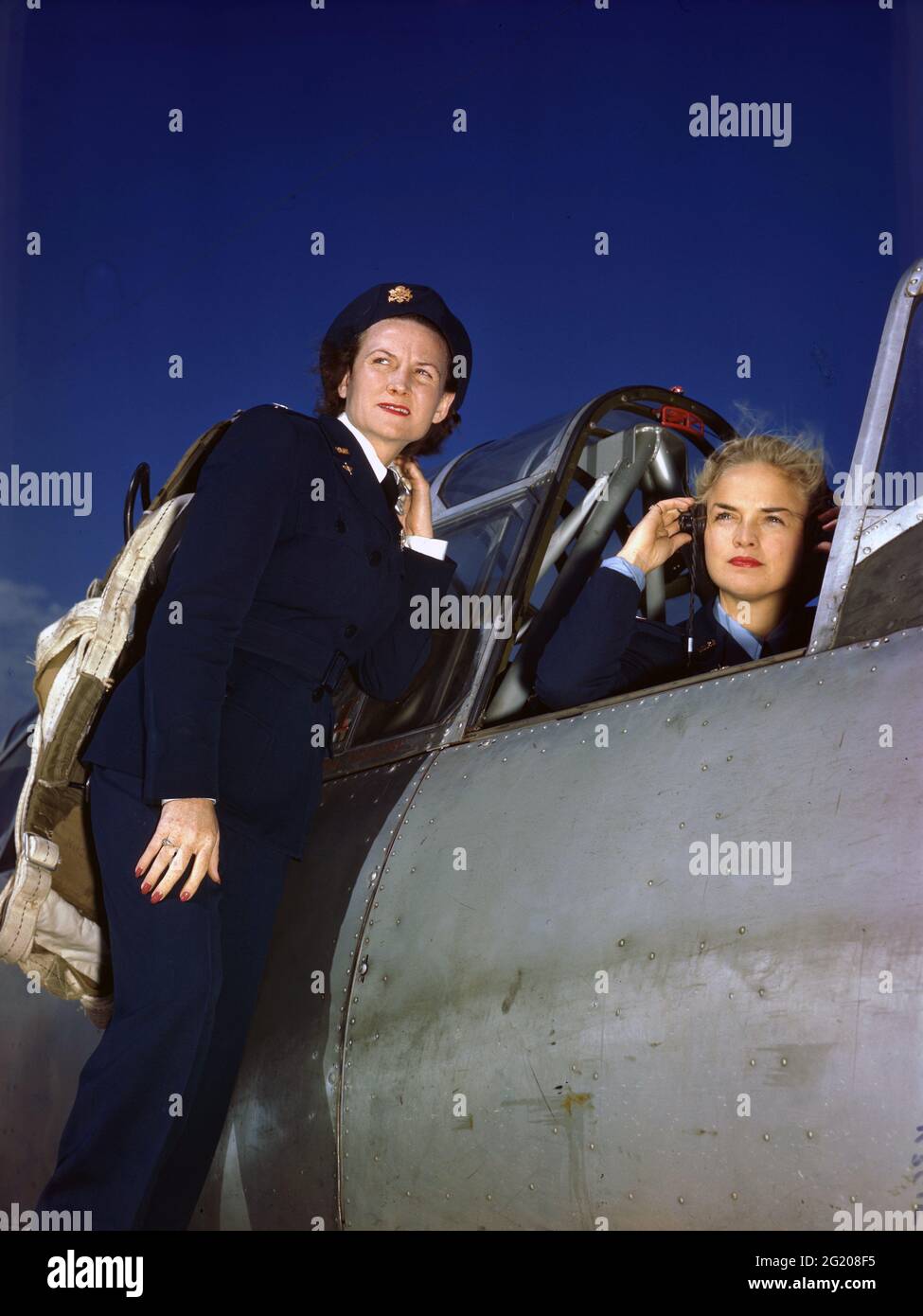 Anne McClellan, die Luftwaffenpilotin der Frauen, passt ihre Kopfhörer im Cockpit eines BT-13 an, während Ann Johnson um 1944 auf dem Flügel des Flugzeugs ohne Standort steht. (Foto der US Army Air Force/RBM Vintage Images) Stockfoto