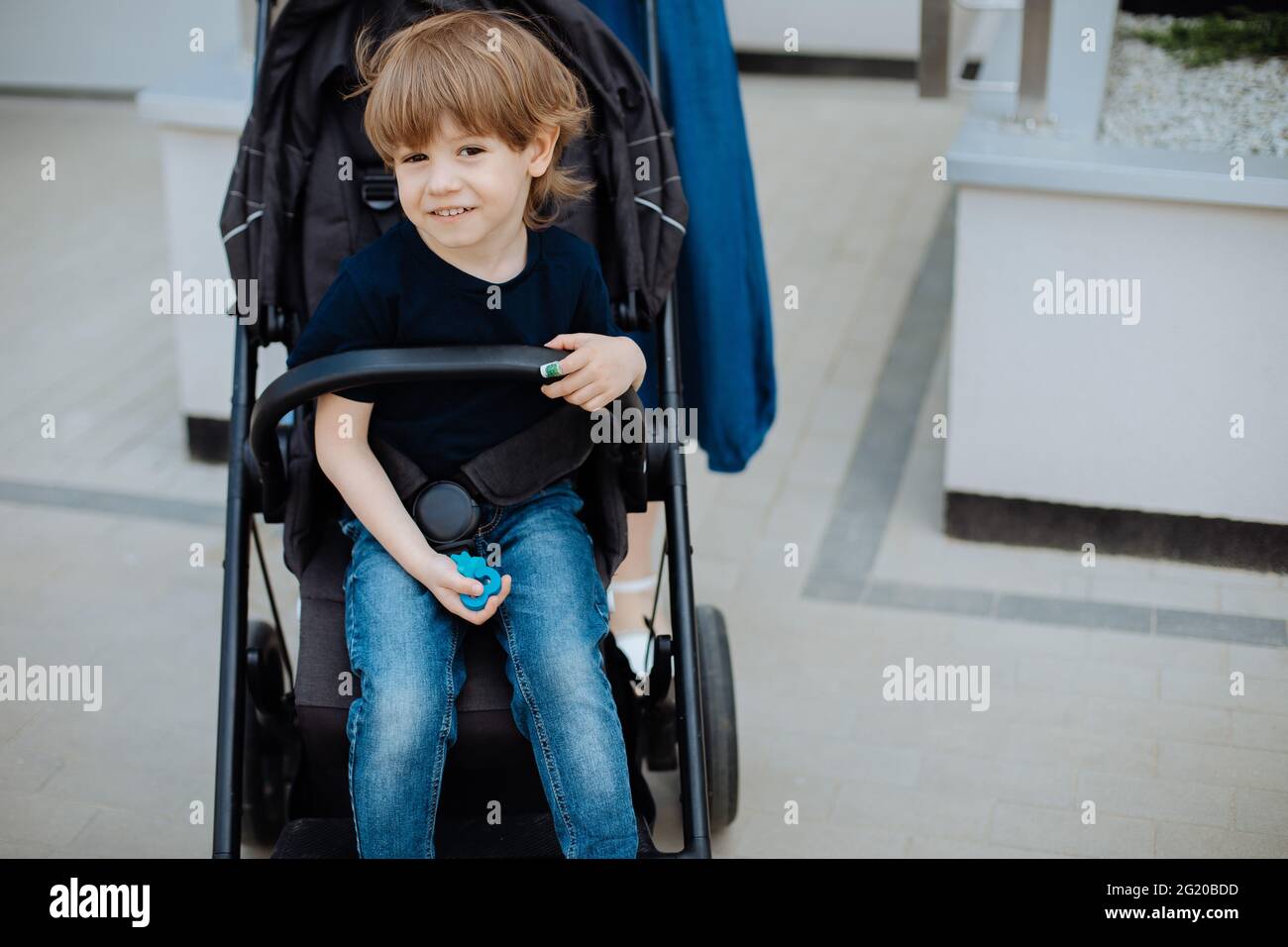 Porträt des Jungen 3 Jahre alt in Babywagen, blickt auf Kamera und lächelt. Kindheit und Unachtsamkeit Stockfoto