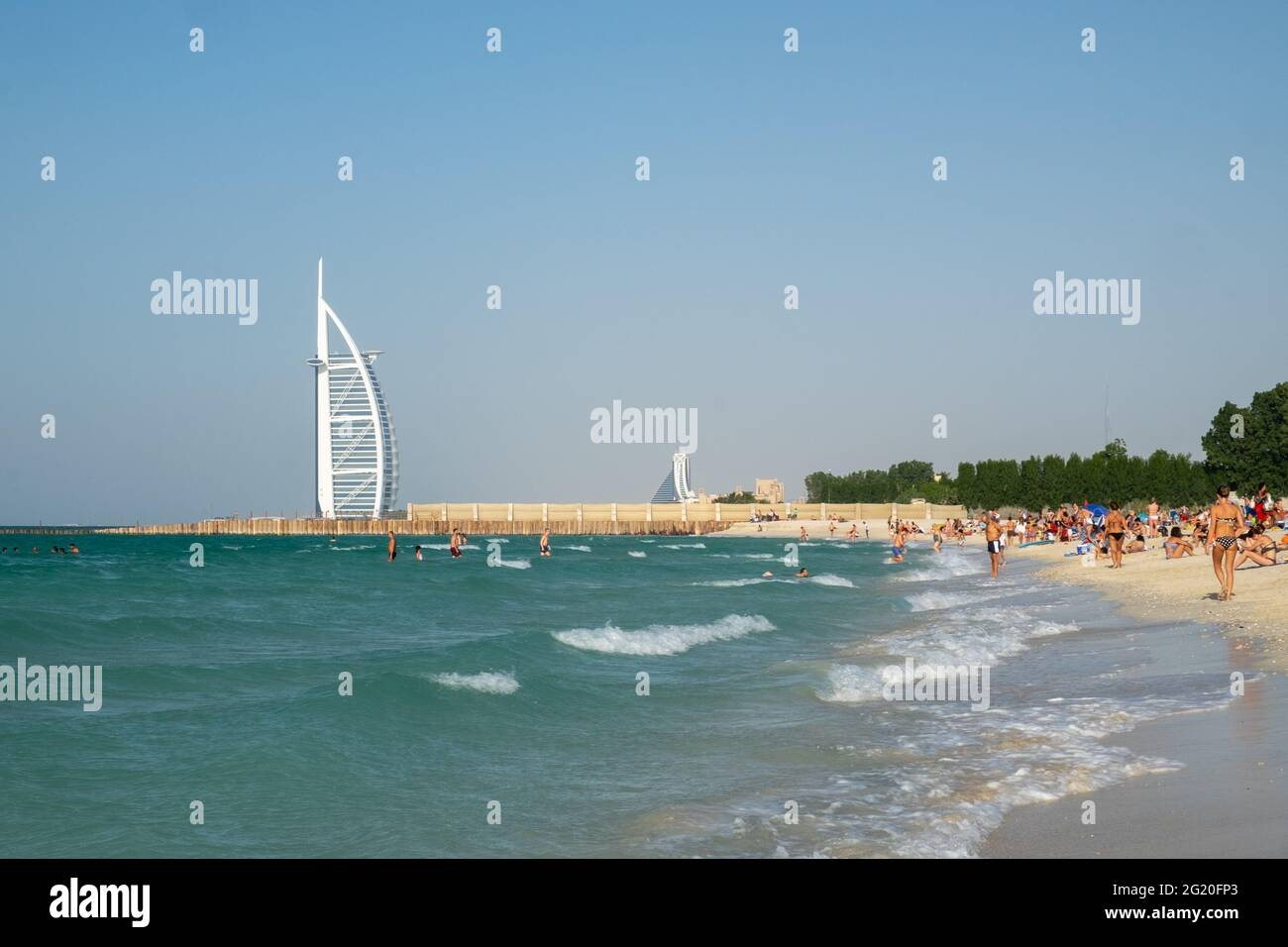 Menschen am Strand mit dem weißen Segel von Burj Al Arab in der Ferne sichtbar. Dubai, VAE. Stockfoto