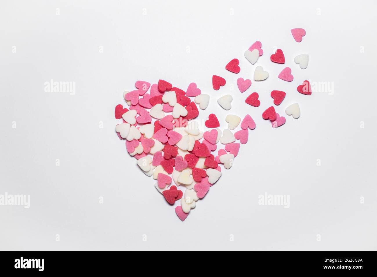 Süße Herzen. Rosa, rote und weiße herzförmige Zuckerstreuseln. Bunte kleine Herzen fliegen ab. Hintergrund oder Karte zum Valentinstag oder Muttertag. Stockfoto