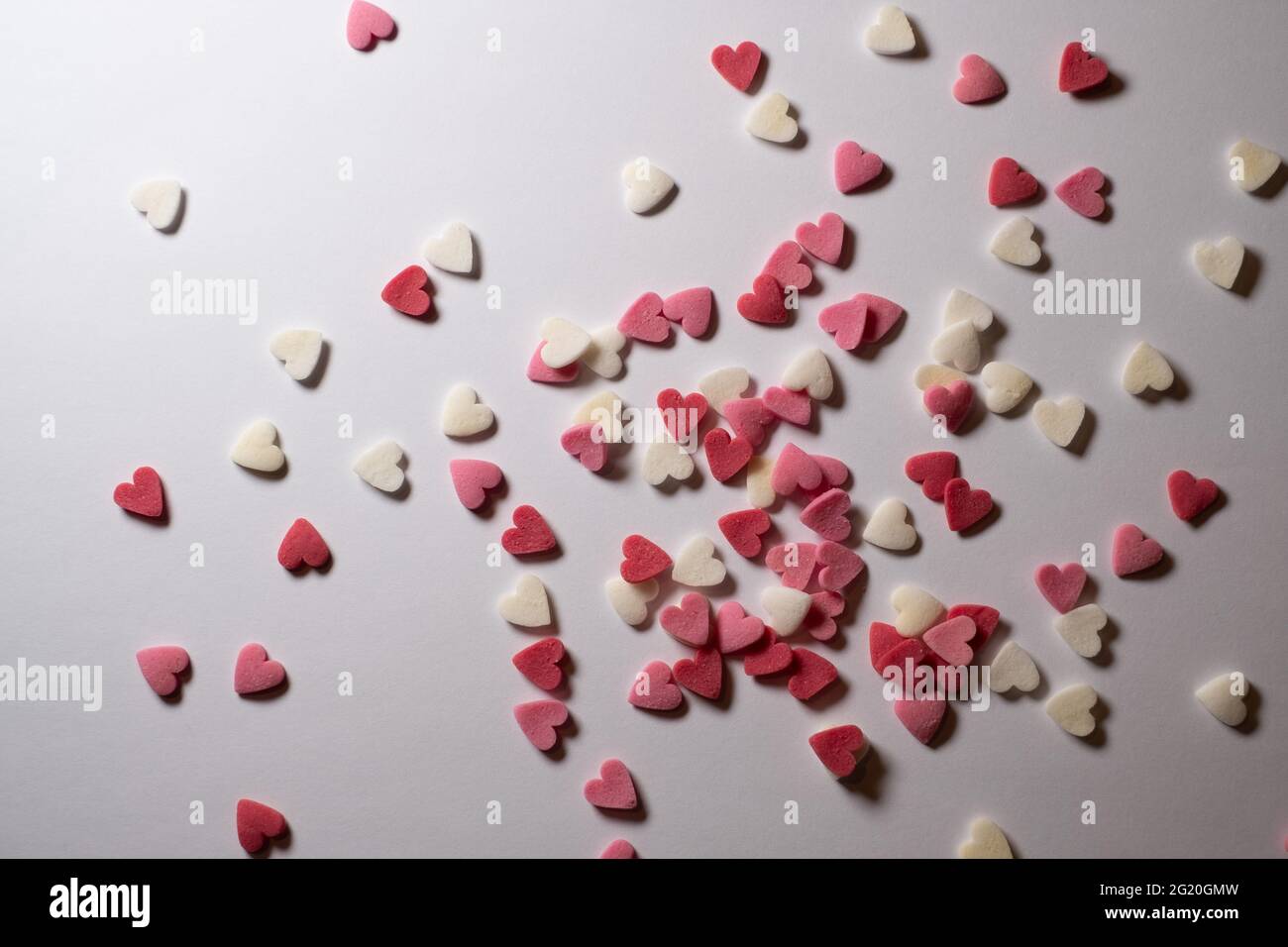 Süße Herzen. Rosa, rote und weiße herzförmige Zuckerstreuseln. Buntes Herz aus vielen kleinen Herzen. Valentinstag oder Muttertag Hintergrund Stockfoto