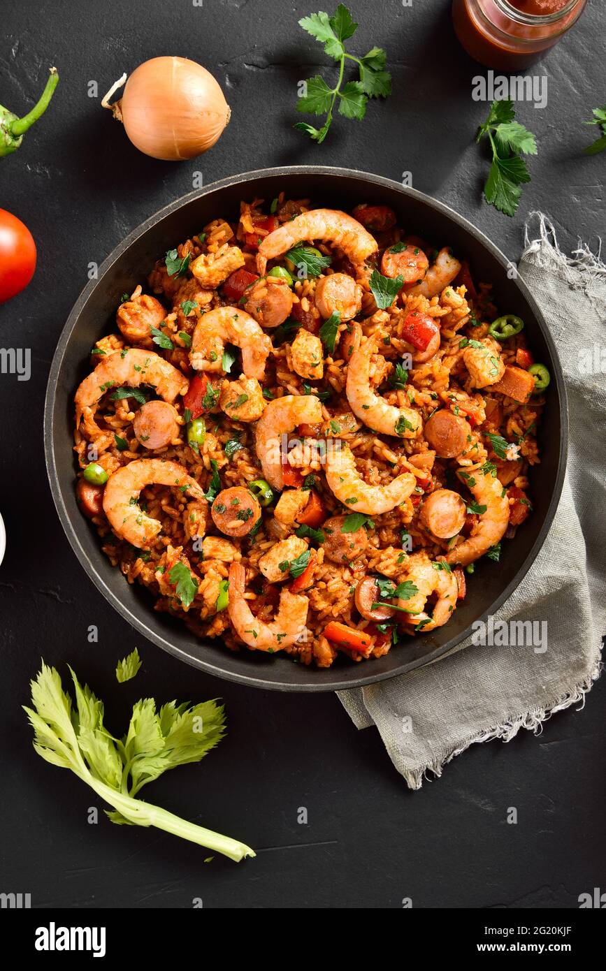 Kreolischer Stil Jambalaya mit Huhn, geräucherten Würstchen und Gemüse in Bratpfanne auf schwarzem Stein Hintergrund. Draufsicht, flach liegend, Nahaufnahme Stockfoto