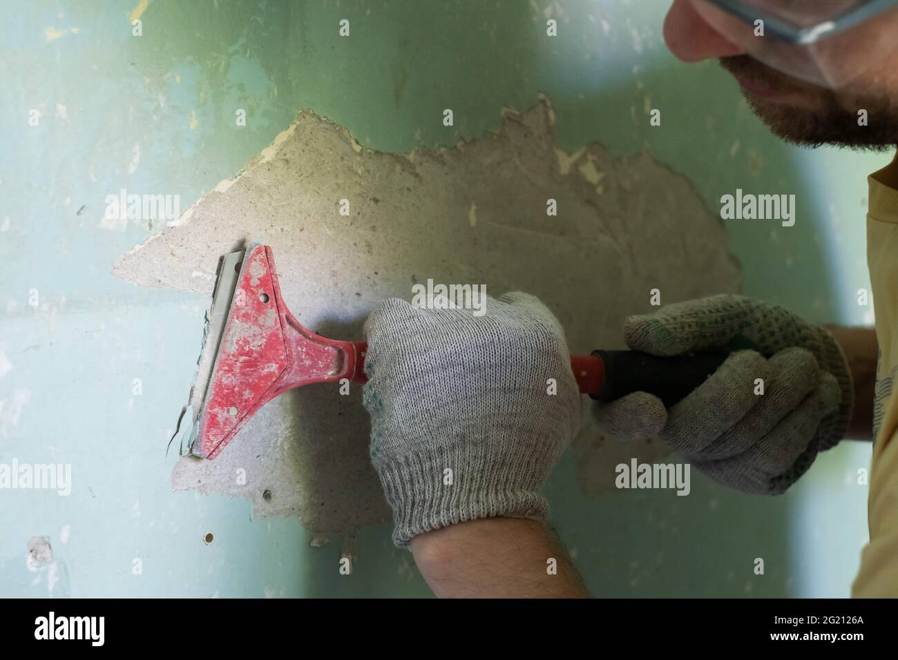 Kaukasischer Mann, der alte Farbe mit einem Schaber entfernt. Stockfoto