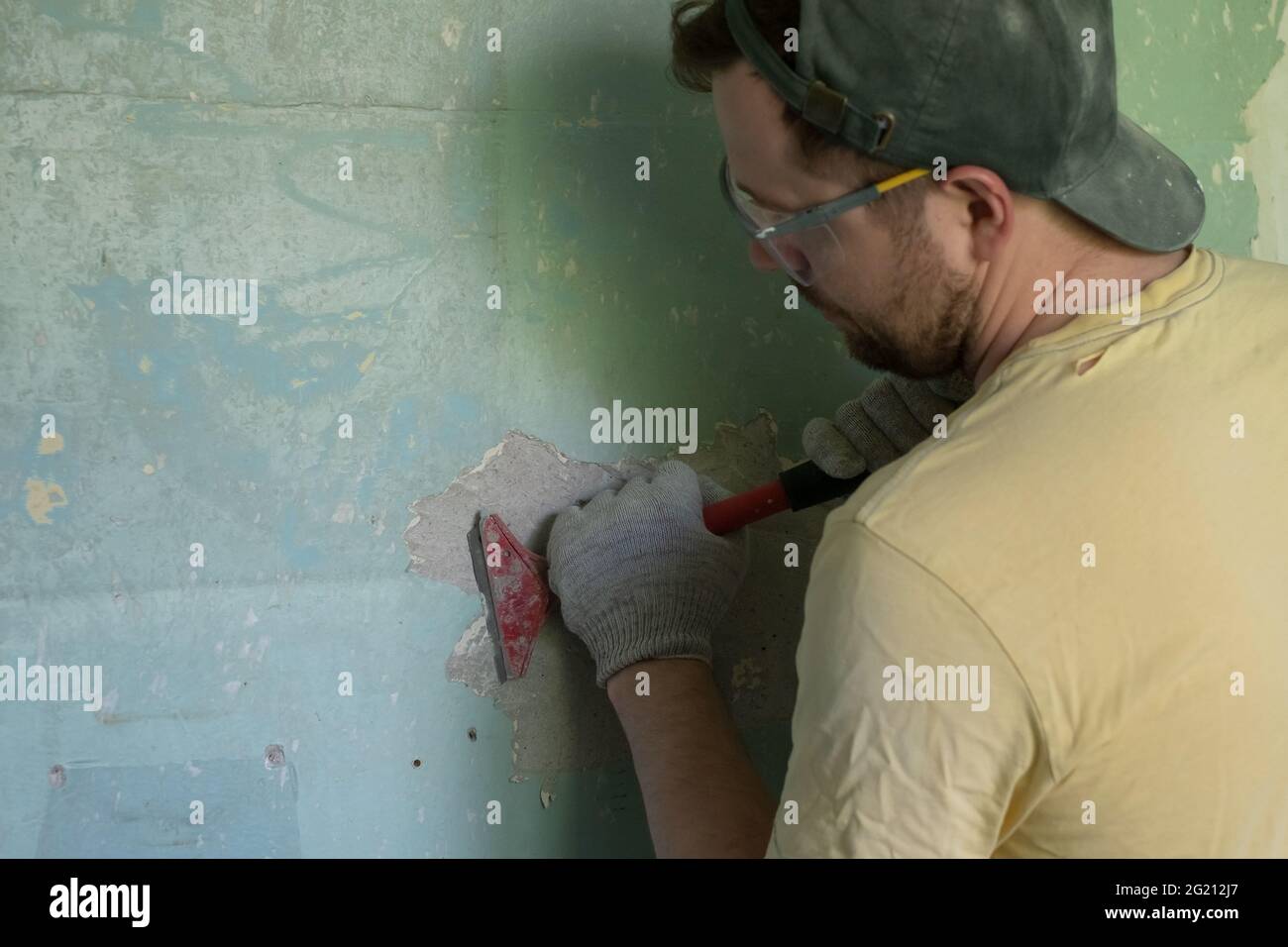 Kaukasischer Mann, der alte Farbe mit einem Schaber entfernt. Stockfoto