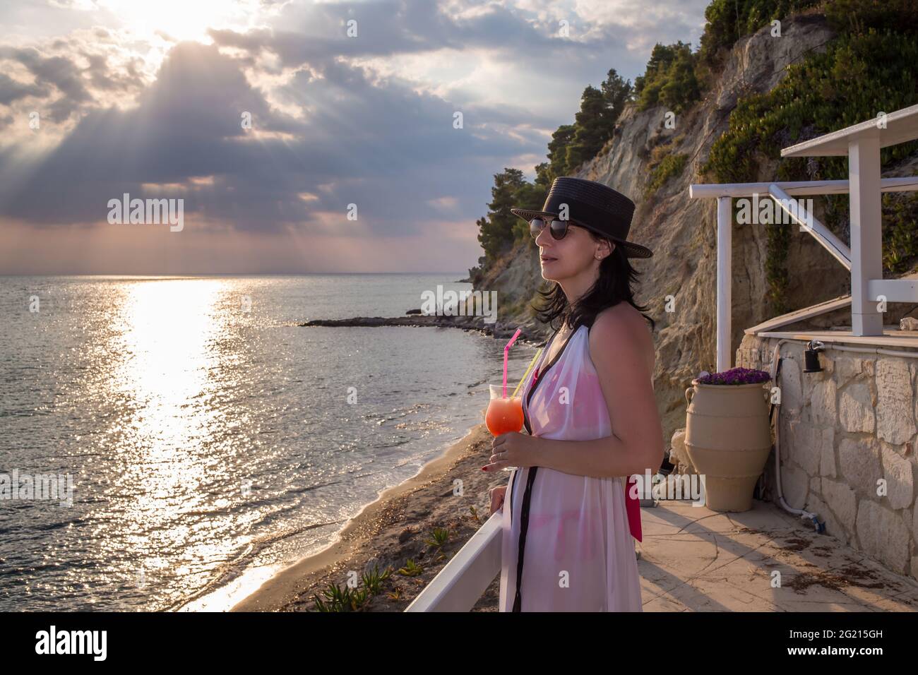 Eine wunderschöne Frau mittleren Alters trinkt Cocktails auf einer Terrasse beim Meer Stockfoto