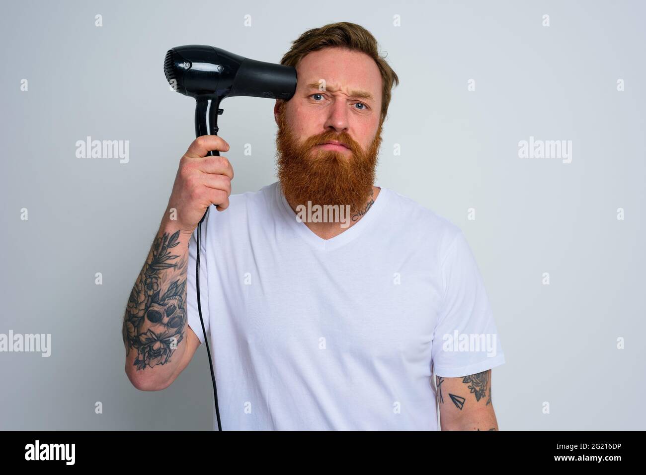 Unglücklicher Mann mit Bart spielen mit Haaren dryeras eine Pistole Stockfoto