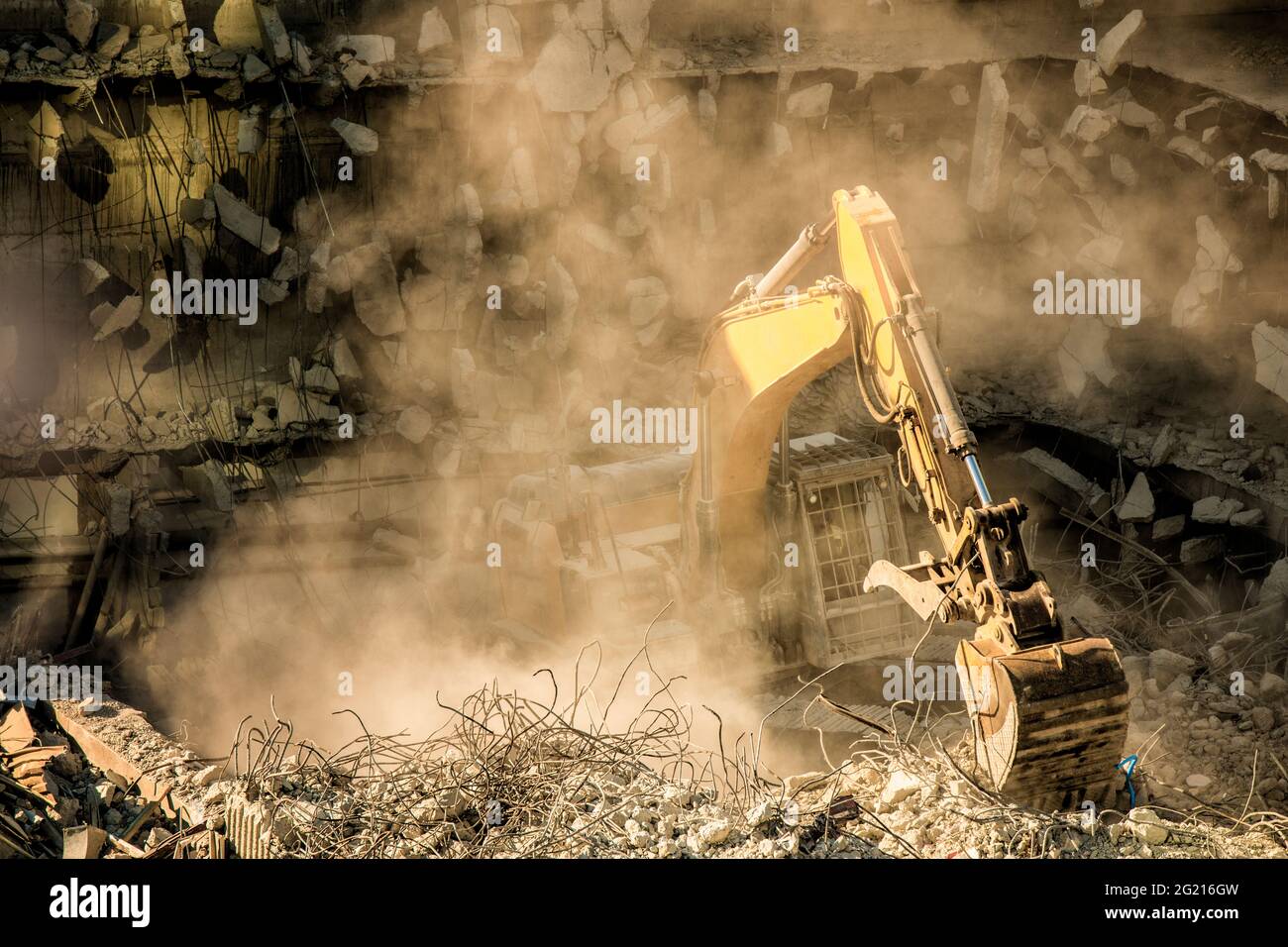 Baumaschinen, Bagger, Bulldozer, Reinigung von Trümmern und Schutt nach dem Abriss eines alten Gebäudes, umgeben von einer Staubwolke Stockfoto