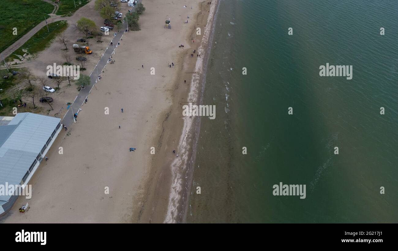 Luftaufnahme von Sandstrand und Meer an einem bewölkten Frühlingstag. Die Leute laufen am Strand entlang Stockfoto