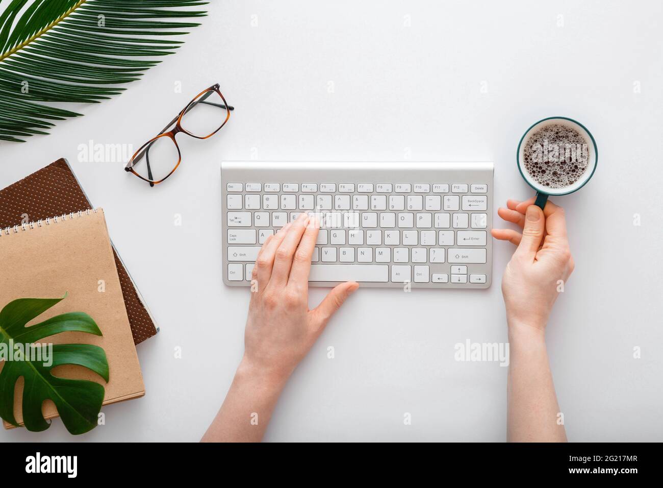 Frau tippt auf der Computertastatur und trinkt Kaffee am Arbeitsplatz. Flacher Büroarbeitsplatz mit weiblichen Händen auf weißem Hintergrund Stockfoto