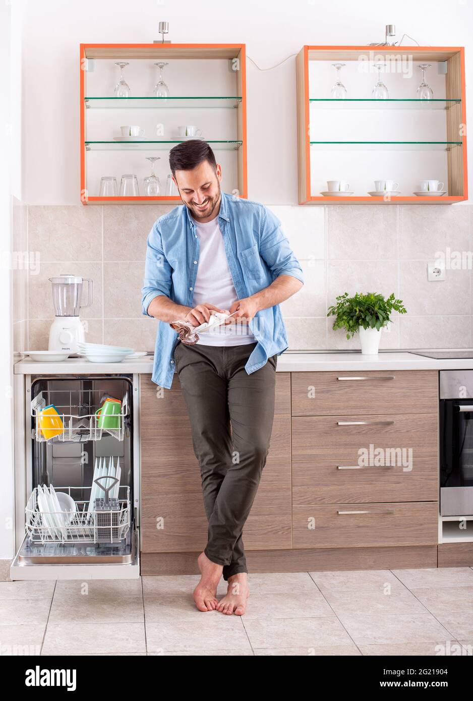 Junger Mann in der Küche tut Hausarbeiten Reinigung Geschirr wischen. Attraktiver Mann Polierplatte lächelt glücklich. Stockfoto