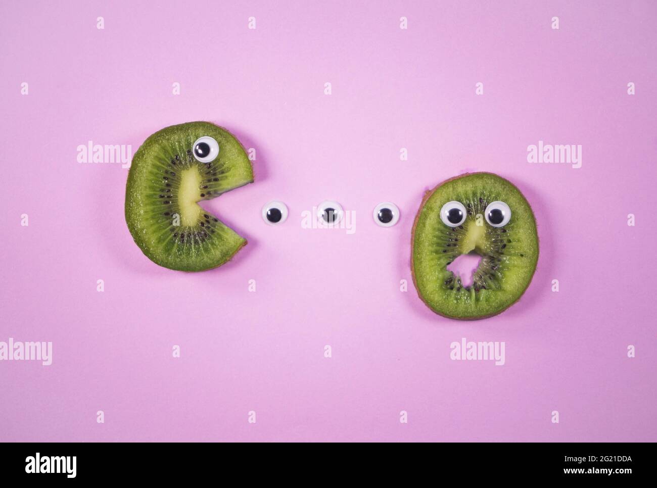 Kiwi-Scheiben mit Spielzeugaugen auf trendigem, weichen rosa Hintergrund. Lustige und beängstigende Essenszene. Halloween-Idee. Tropische Früchte und Sommerkonzept. Stockfoto