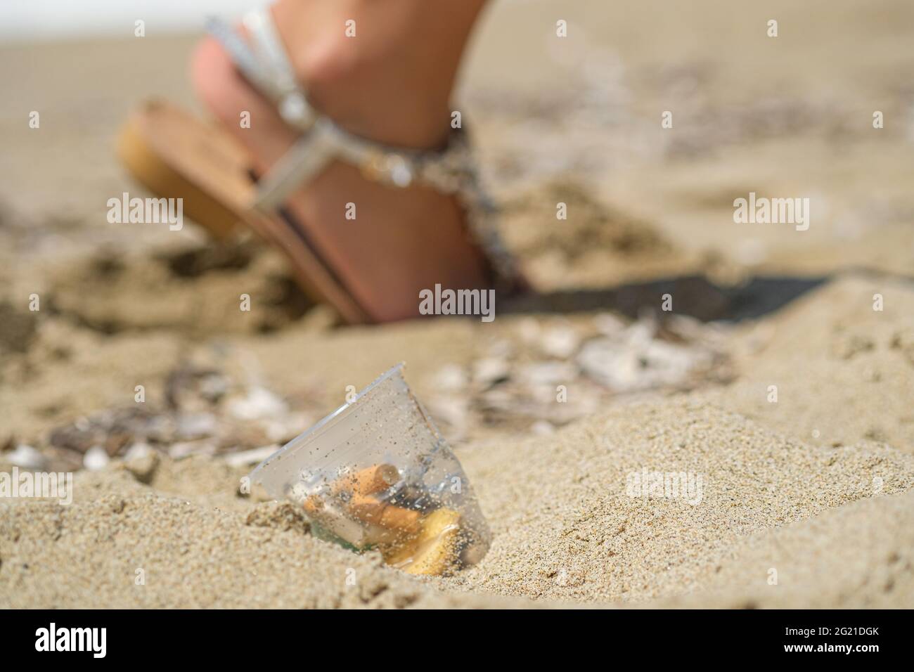 Plastikbecher auf Meeresküsten Ökosystem mit Frau zu Fuß auf Hintergrund verworfen, Natur Abfall Verschmutzung Stockfoto