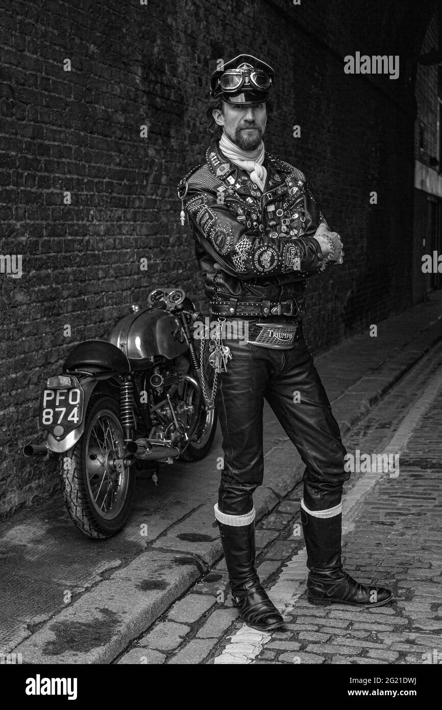 Rocker in Cafe Racer-Ausrüstung trägt schwarze Lederjacke mit Nieten, Patches und Abzeichen klassischen britischen Motorrad in London, Großbritannien bedeckt Stockfoto