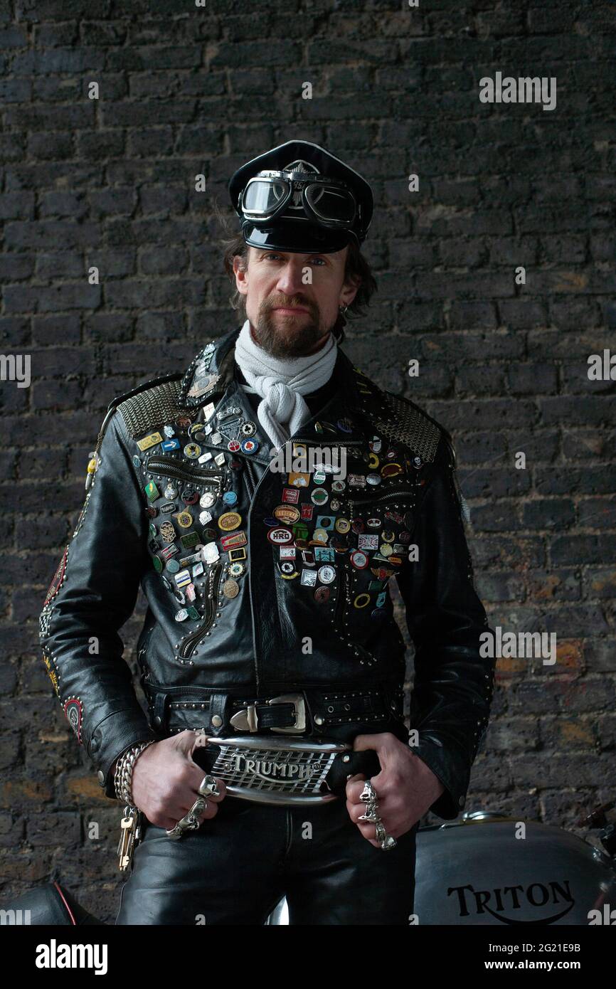 Rocker in Cafe Racer-Ausrüstung trägt schwarze Lederjacke mit Nieten, Patches und Abzeichen klassischen britischen Motorrad in London, Großbritannien bedeckt Stockfoto