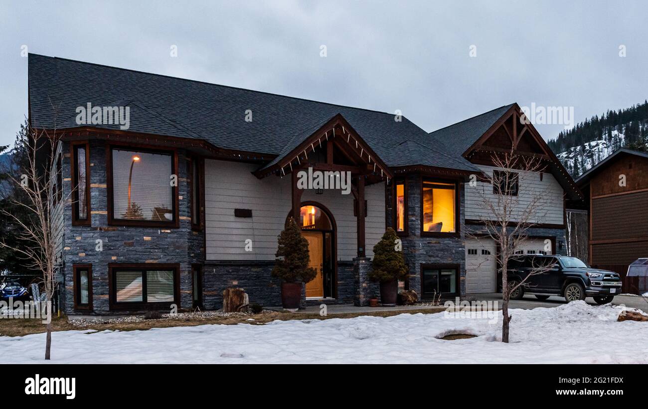 REVELSTOKE, KANADA - 14. MÄRZ 2021: Privathaus und Straßenansicht in Kleinstadt Abendzeit früher Frühling mit Schnee Stockfoto