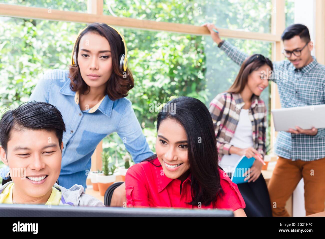 Kreative engagierte junge Mitarbeiter, die moderne Technologien einsetzen, während sie an verschiedenen Projekten im Büro arbeiten Stockfoto