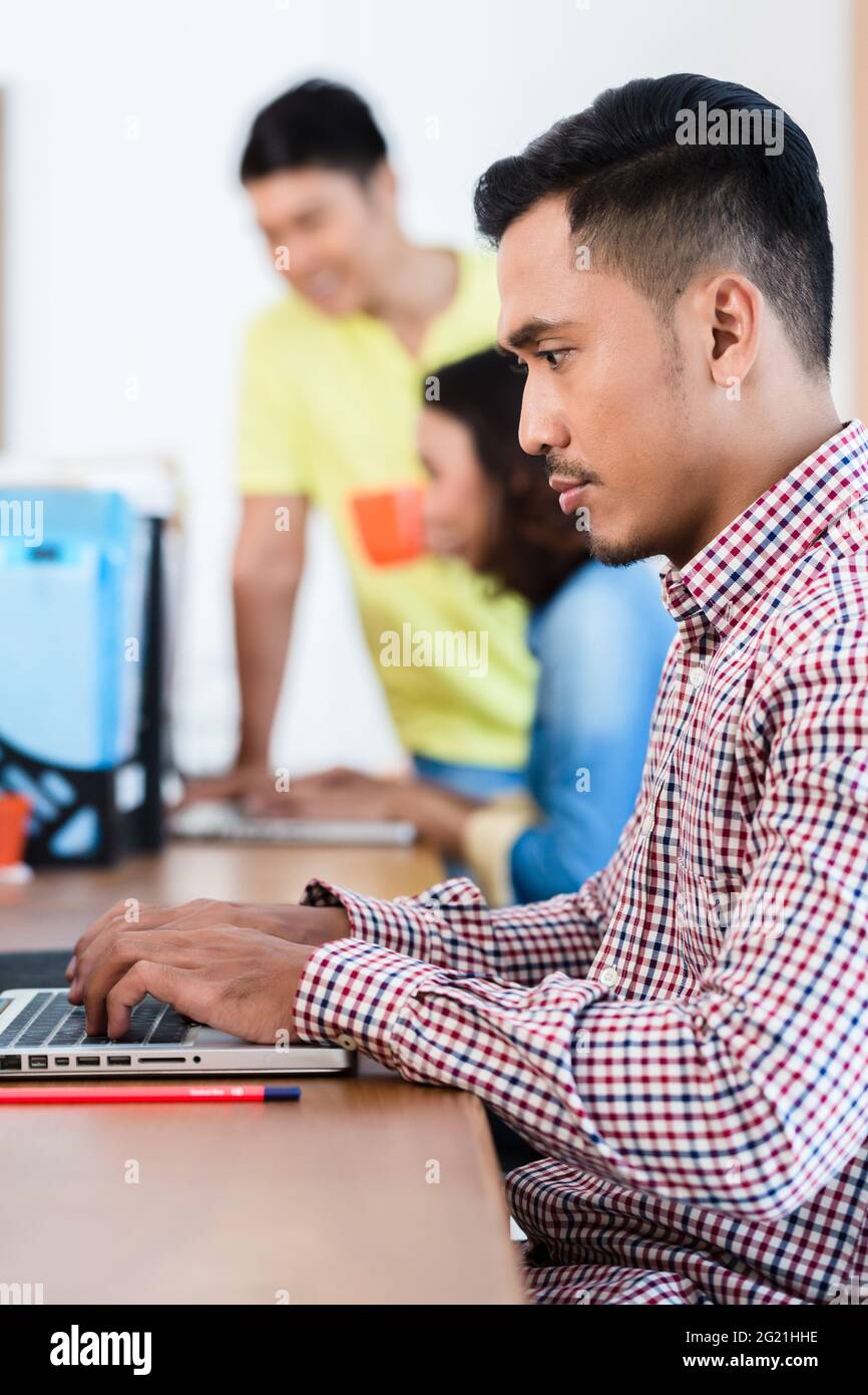 Seitenansicht eines jungen engagierten asiatischen Experten, der an seinem Schreibtisch sitzt, während er im Büro an einem Laptop arbeitet Stockfoto