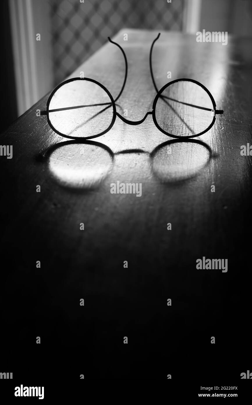 Eine altmodische Vintage-Brille mit Drahtrahmen, durch die Licht auf einem alten schwarzen und weißen Holztisch mit Platz zum Kopieren durchscheint. Stockfoto