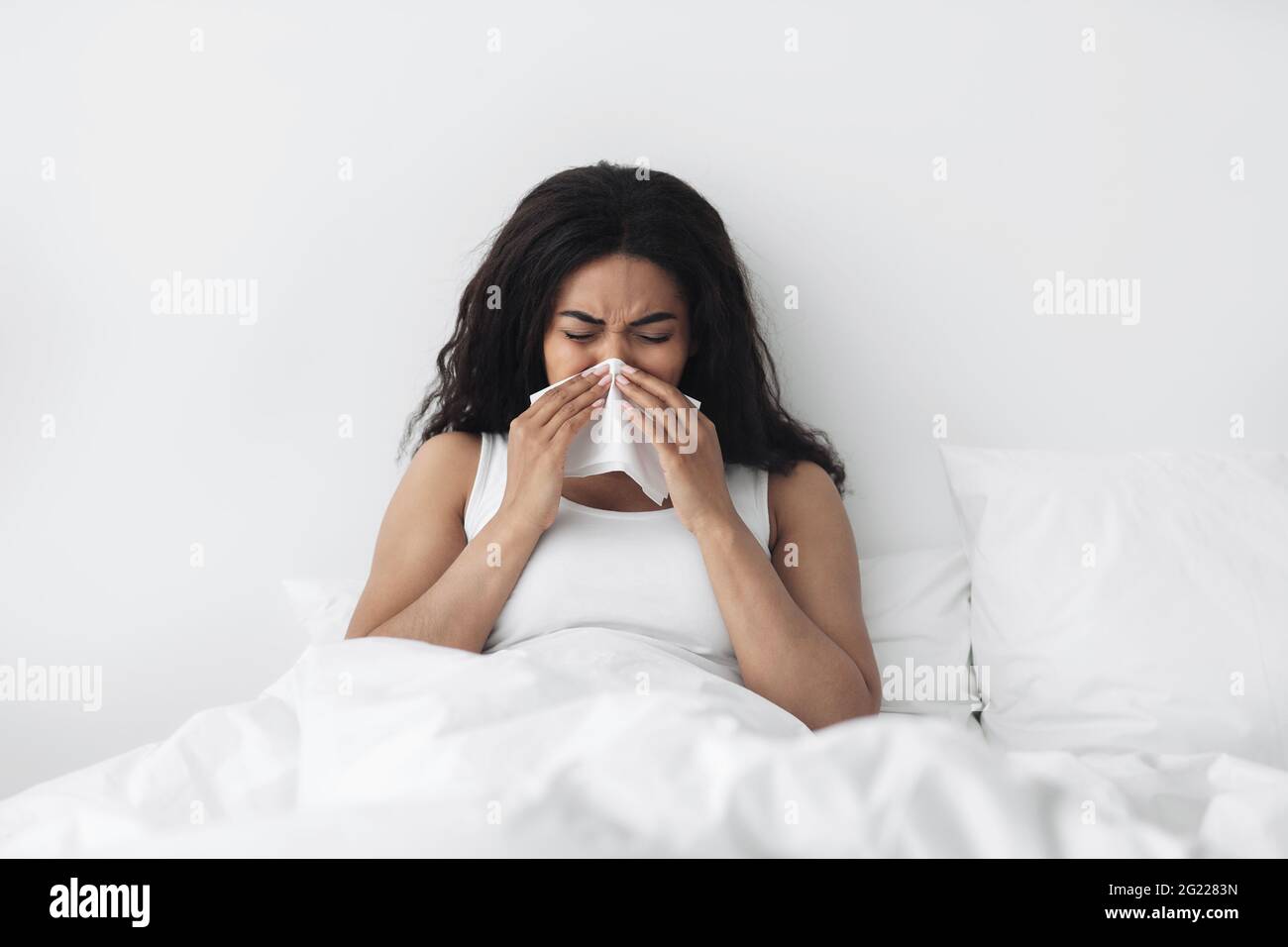 Laufende Nase, Grippe und Erkältungen. Kranke afroamerikanische Dame, die im Bett liegt und mit Serviette in die Nase bläst Stockfoto