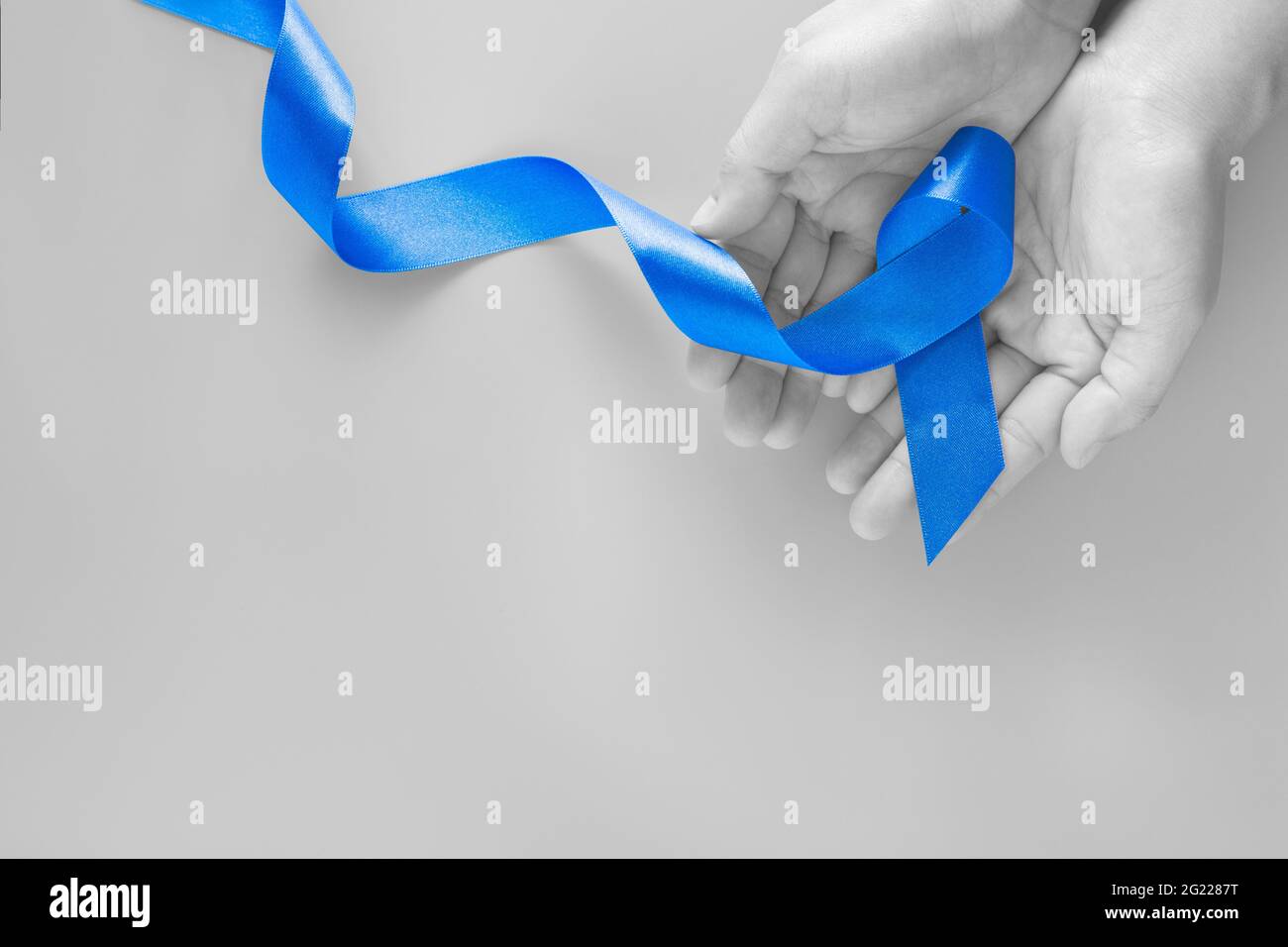 Hände halten tiefblaues Band auf blauem Hintergrund mit Kopierraum. Darmkrebs Bewusstsein Kolonenkrebs von älteren Menschen und Welt Diabetes Tag CHI Stockfoto