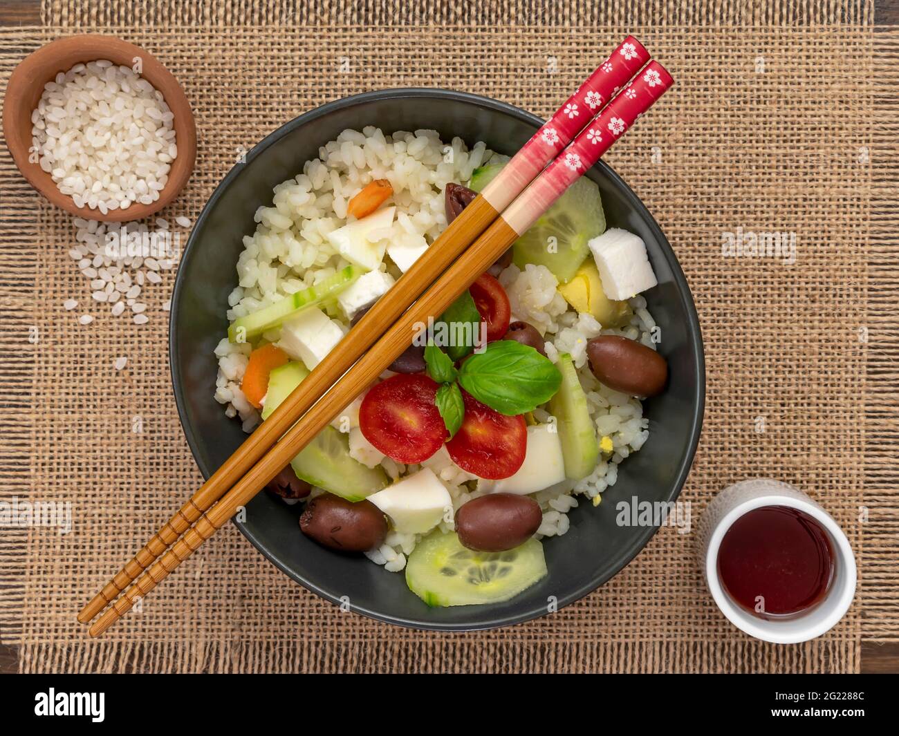 Ein kalter Reissalat auf einer Jute-Matte mit orientalischen Essstäbchen aus Holz auf der Schüssel Stockfoto