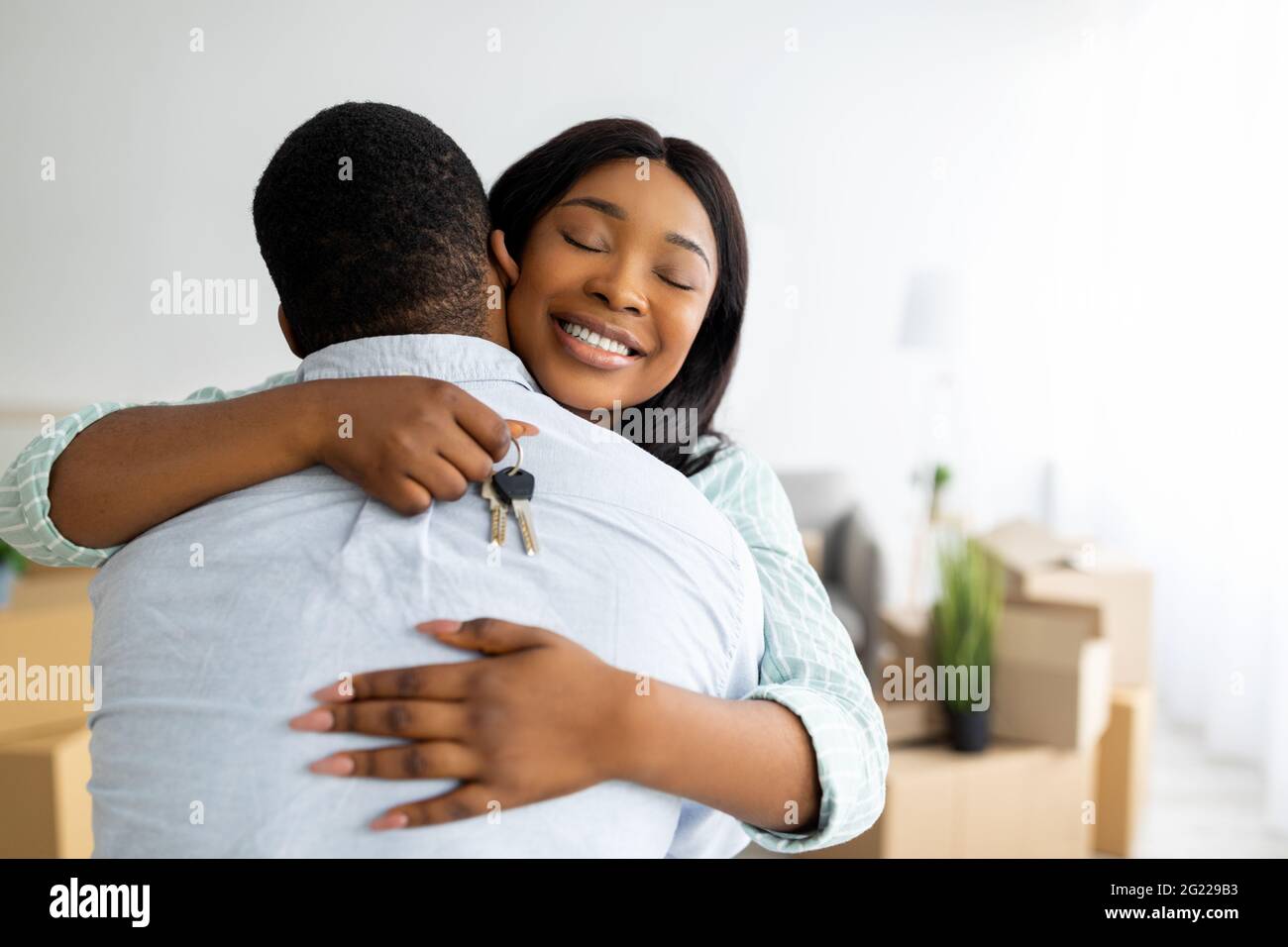 Hauseigentumskonzept. Aufgeregt schwarze Frau hält Hausschlüssel und umarmt ihren Mann, freien Platz Stockfoto