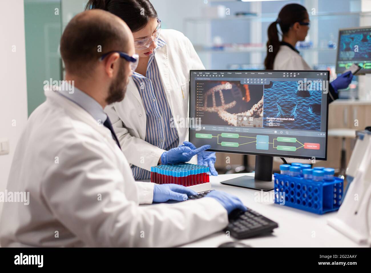 Gruppe von Wissenschaftlern, die in modern ausgestatteten Labor zeigt auf Computer-Desktop. Y zeigt auf Computer-Desktop. Chemiker analysieren die Virusentwicklung mithilfe von Hightech-Technologien für die Behandlungsforschung. Stockfoto