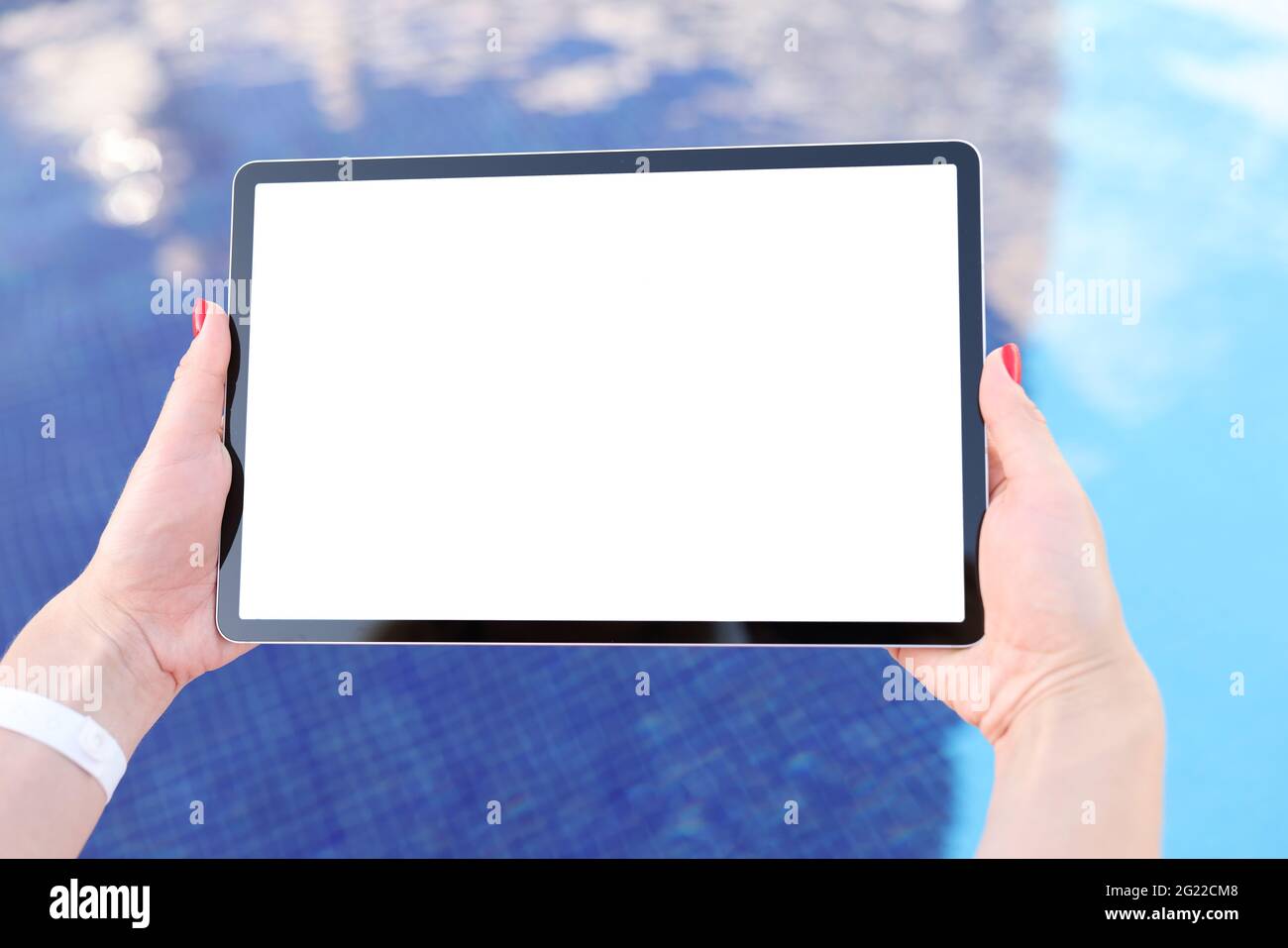 Weibliche Hände halten das Tablet mit einem weißen Bildschirm über dem Wasser des Pools Stockfoto