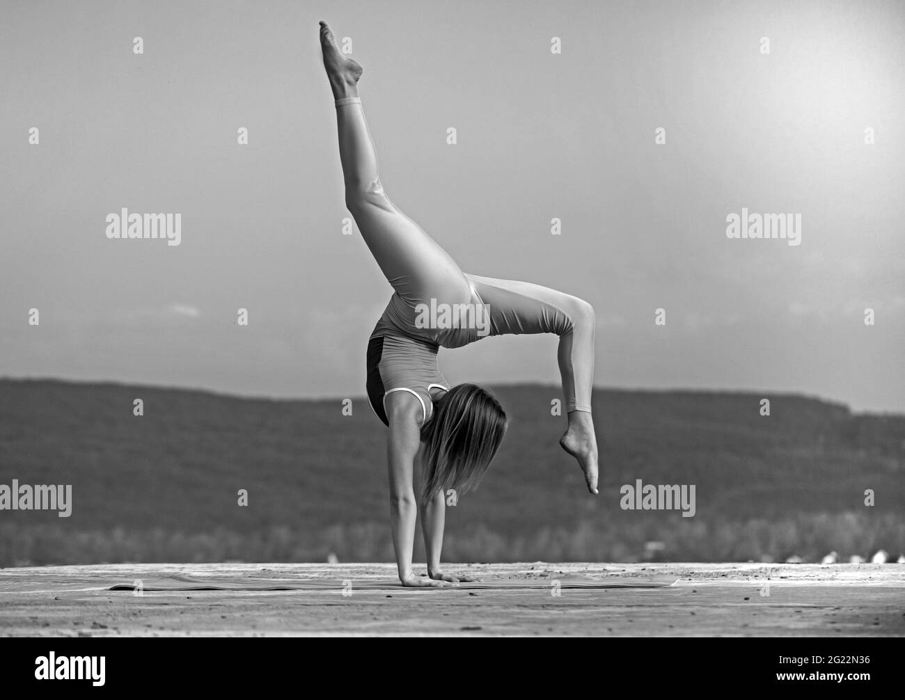 Schöne athletische Frau dehnt sich und macht eine Brücke auf Himmel Hintergrund. Stockfoto