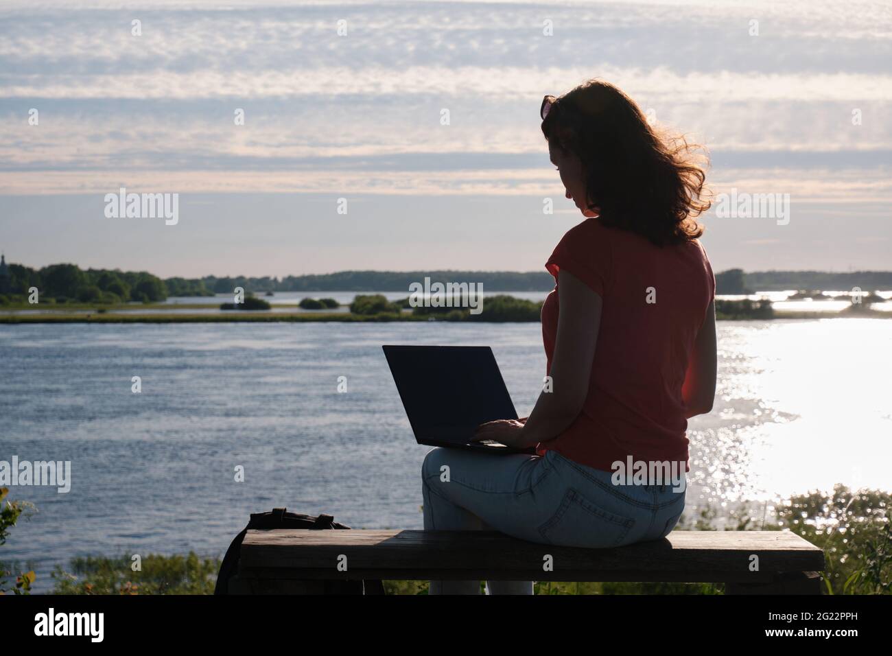 Das Mädchen sitzt auf einer Bank und benutzt einen Laptop. Kommunikation außerhalb der Stadt. Lager Stockfoto