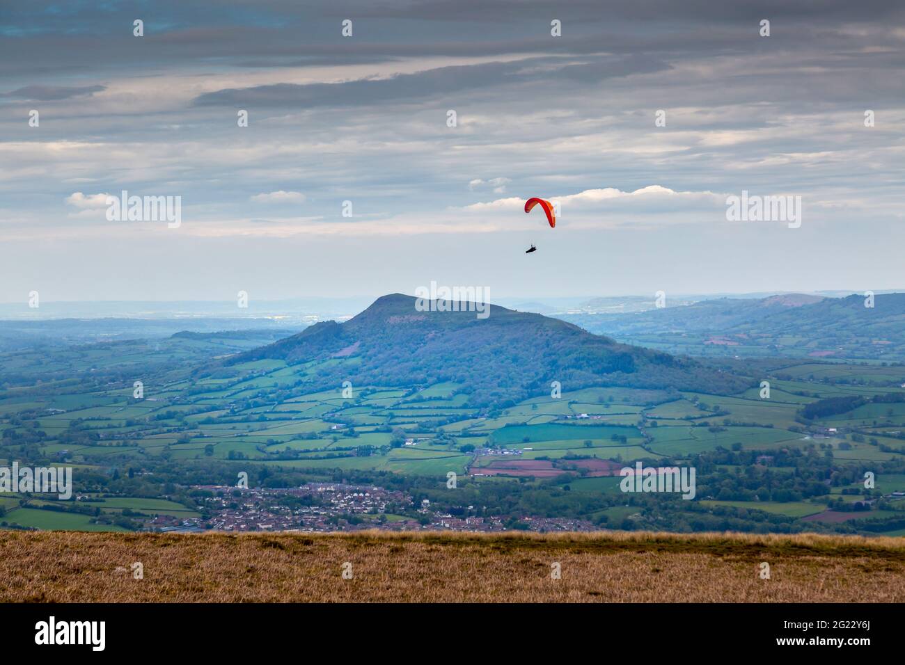 Ein Solo-Gleitschirm flog von der Blorenge hoch über die Felder von Abergavenny mit dem Berg Skirrid im Hintergrund. Stockfoto