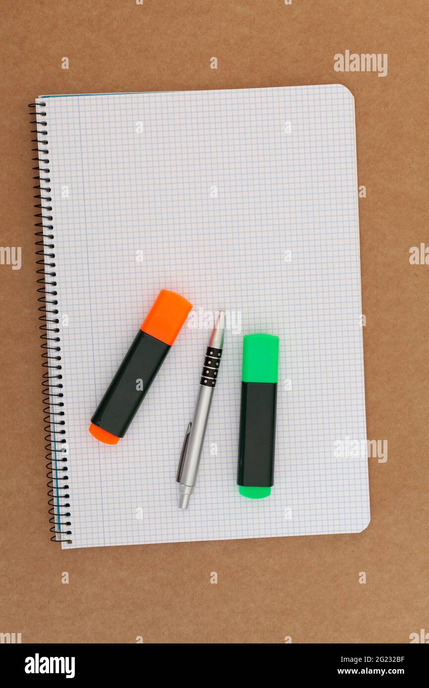 Notizbuch mit Gitterblättern, auf denen sich zwei Marker und ein Stift befinden und der auf einer Kartonoberfläche platziert ist. Die Ausrichtung des Bildes ist vertica Stockfoto