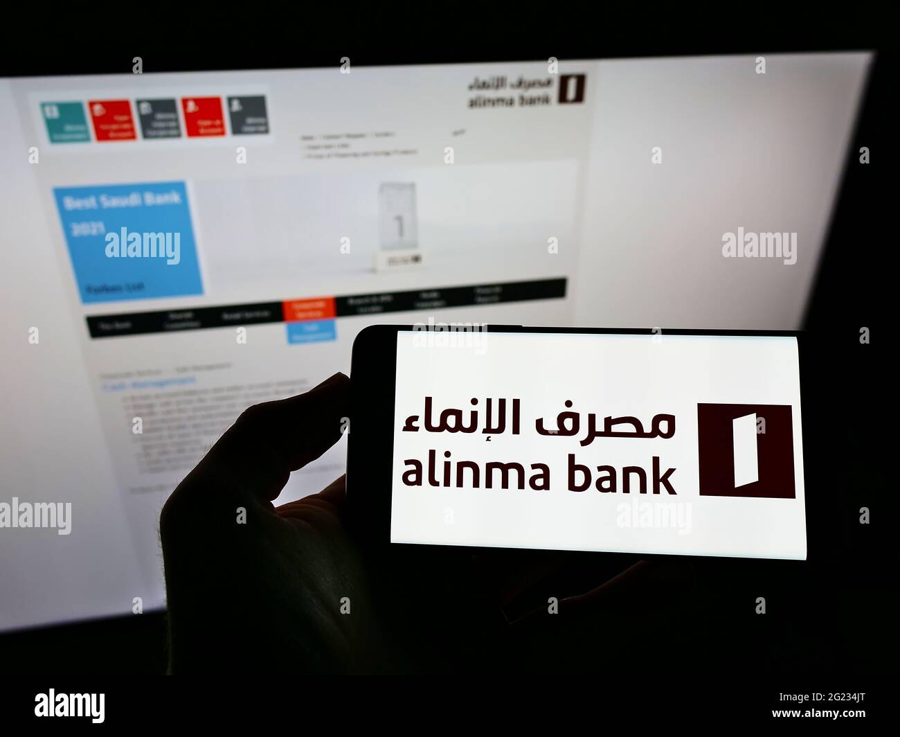 Person, die Mobiltelefon mit dem Logo des Saudi-arabischen Finanzunternehmens Alinma Bank auf dem Bildschirm vor der Business-Webseite hält. Konzentrieren Sie sich auf die Telefonanzeige. Stockfoto