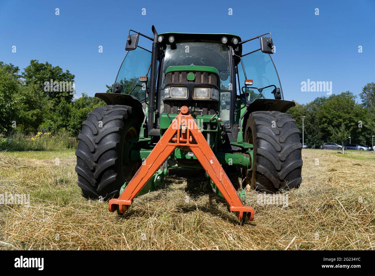 Niedriger Winkel Ansicht des grünen Traktors im Heufeld im Sommer mit offenen Türen und tiefblauem Himmel. Stockfoto