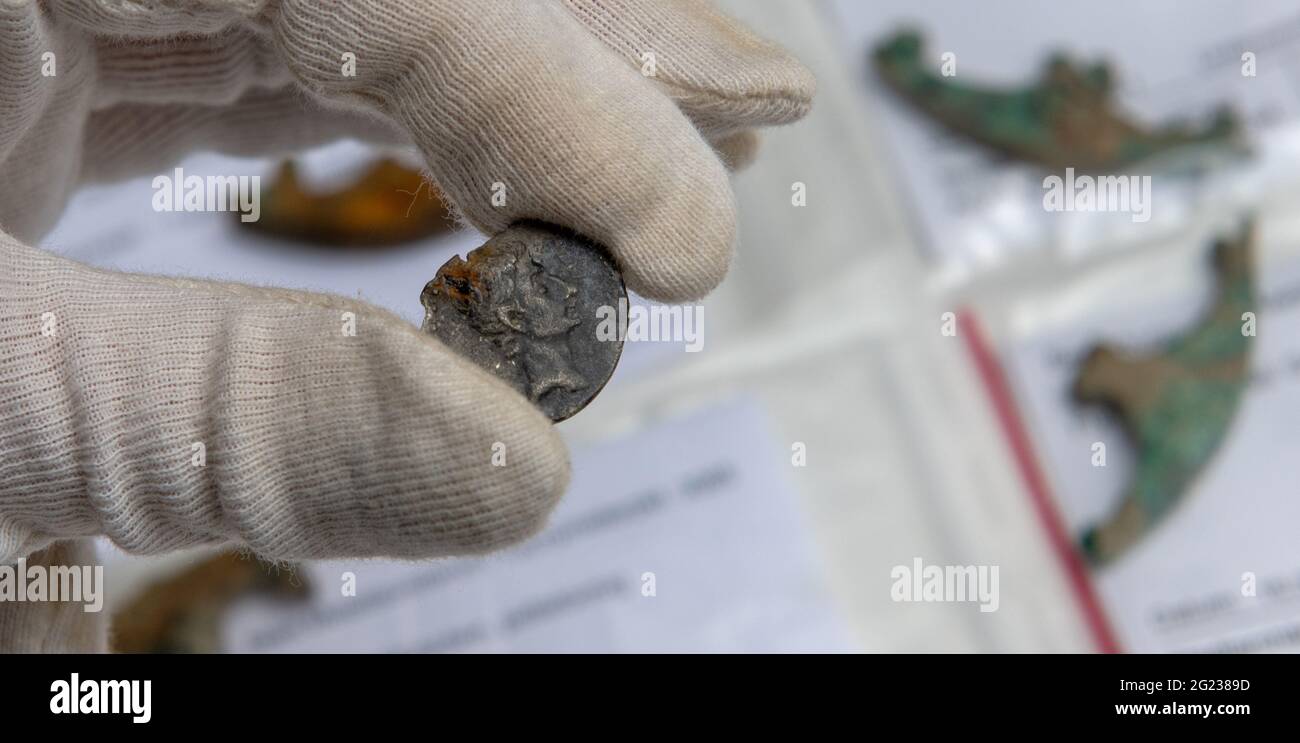 Augsburg, Deutschland. Juni 2021. Ein Angestellter der Abteilung für Archäologie der Stadt hält eine Münze, die Kaiser Augustus darstellt. Es handelt sich um Ausgrabungsfunde aus der Römerzeit, die nach Angaben der Stadt belegen, dass das vor mehr als 2000 Jahren gegründete Augsburger Militärlager die älteste römische Basis im heutigen Bayern ist. Quelle: Stefan Puchner/dpa/Alamy Live News Stockfoto