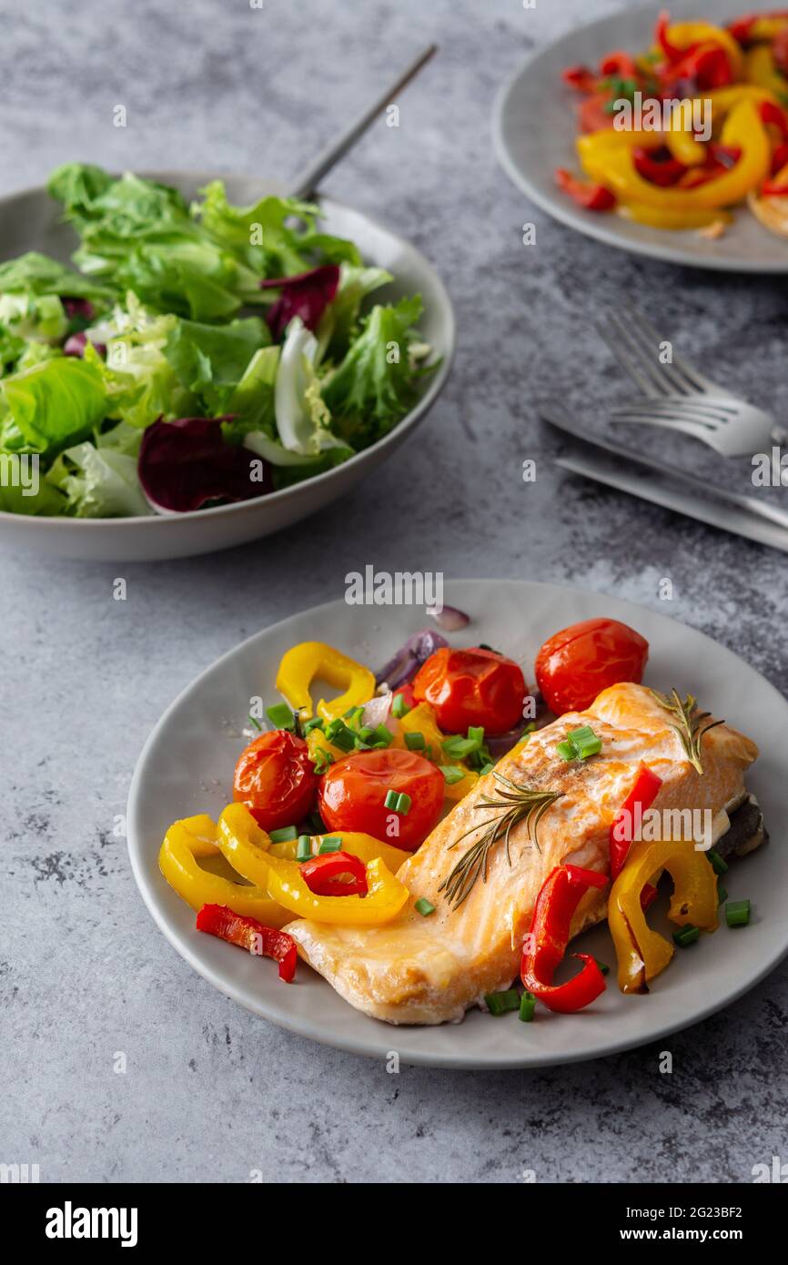 Gebackenes rotes Fischfilet Arctic Saibling auf einem Teller mit Gemüse, Salat in einer Schüssel mischen, leckeres herzhaftes gesundes Abendessen Stockfoto