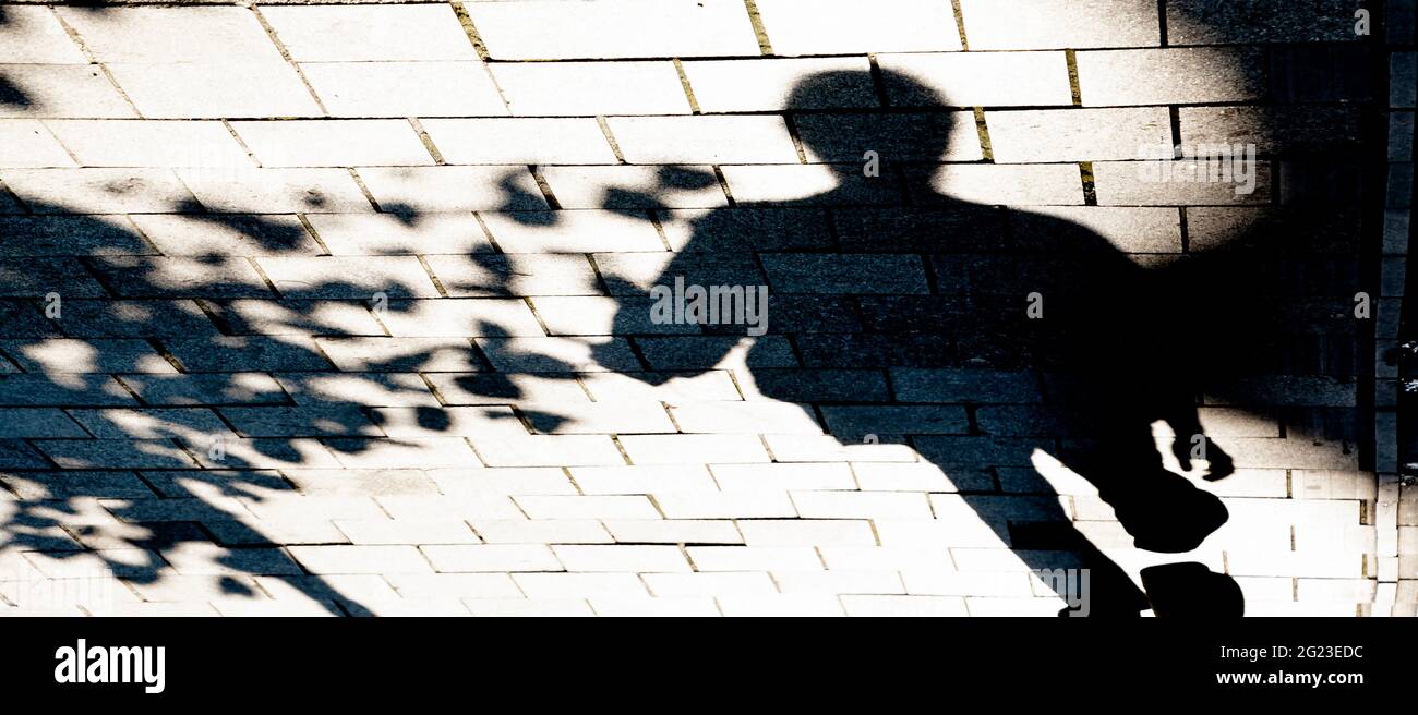 Verschwommene Schattensilhouette einer Person, die am sonnigen Sommertag auf dem Bürgersteig der Stadtstraße läuft, in Schwarz und Weiß Stockfoto