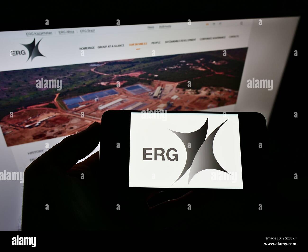 Person mit Mobiltelefon und Logo des Bergbauunternehmens Eurasian Resources Group (ERG) S.à r.l. auf dem Bildschirm vor der Webseite. Konzentrieren Sie sich auf die Telefonanzeige. Stockfoto