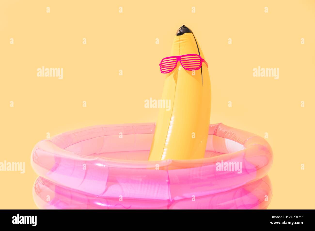Kinderbecken mit einer bananenförmigen aufblasbaren Banane mit Sonnenbrille auf gelbem Hintergrund. Stockfoto