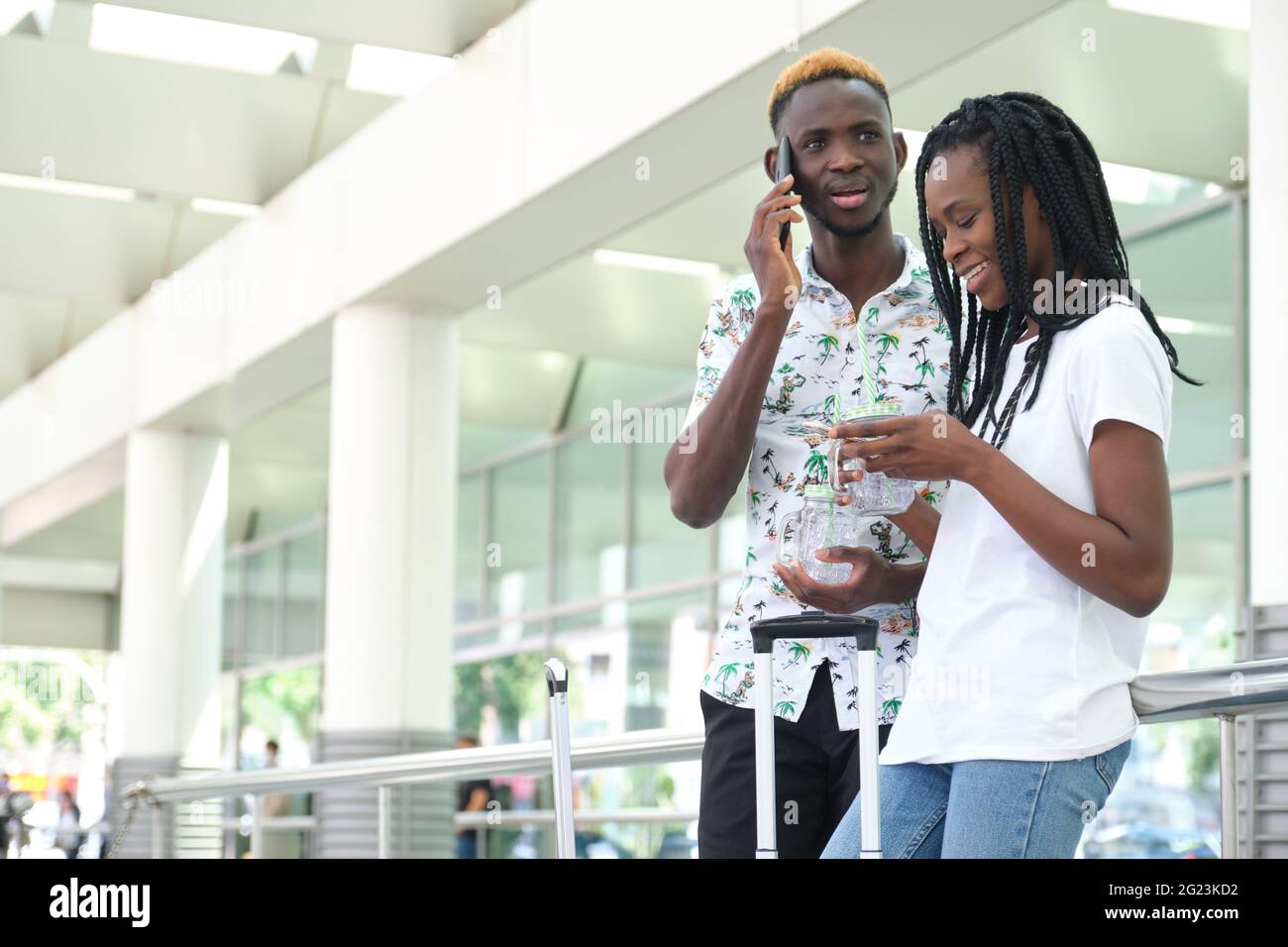 Junges afrikanisches Paar, das sich unterhielt, das Smartphone überprüfte und ein erfrischendes Getränk hielt. Reise- und Sommerkonzepte. Stockfoto