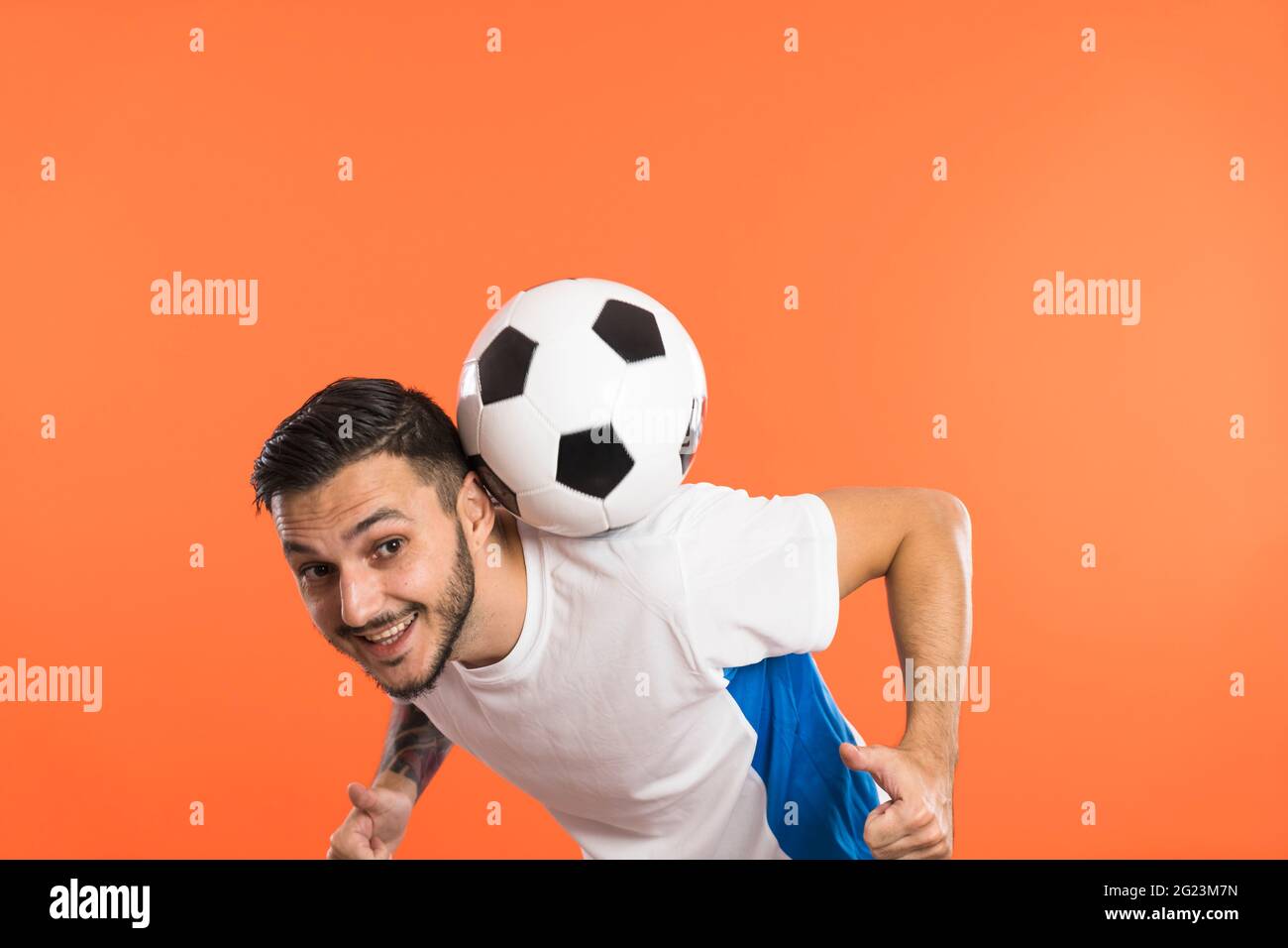 Fußballspieler machen Tricks mit Ball isoliert auf orangefarbenem Hintergrund Stockfoto