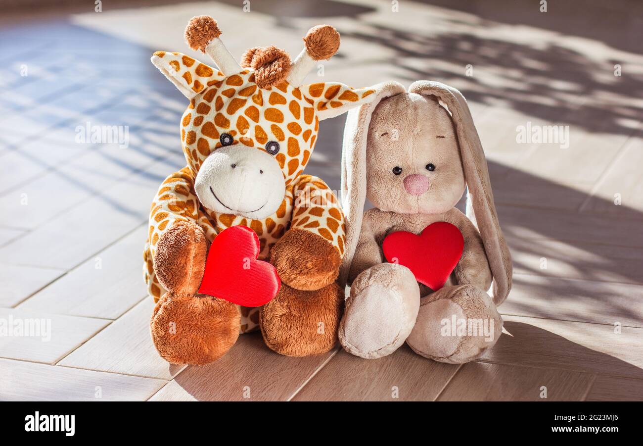 Die weiche Plüsch-Spielzeug-Giraffe und der Hase für Kinder sitzen auf Holzhintergrund, hartem Licht und Schatten Stockfoto