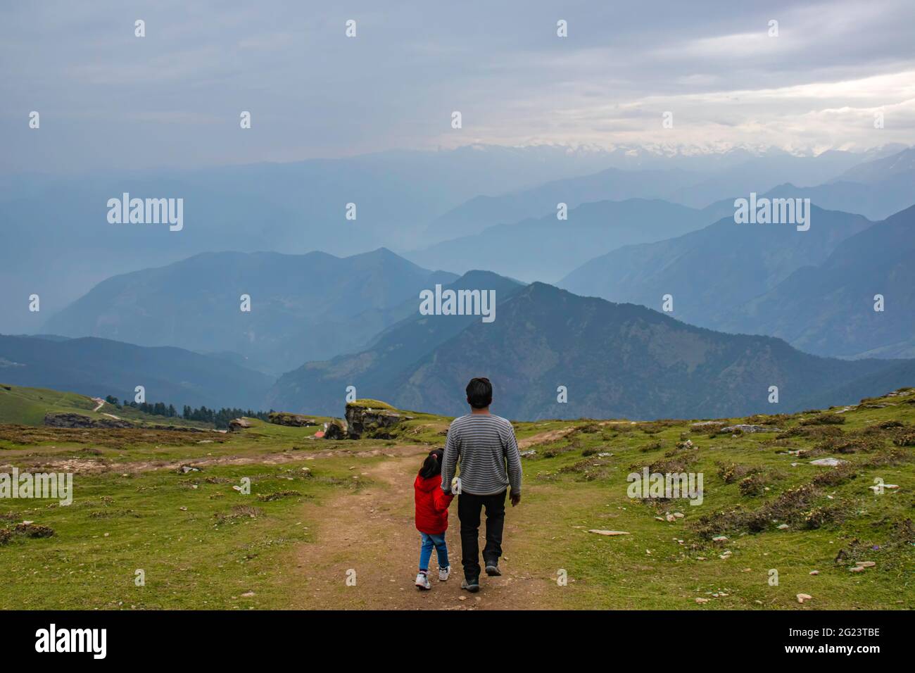 Vater hält die Hand ihres kleinen Mädchens, das sie von den Hügeln mit einem wunderschönen Himalaya-Gebirge vor sich herunternimmt. Stockfoto