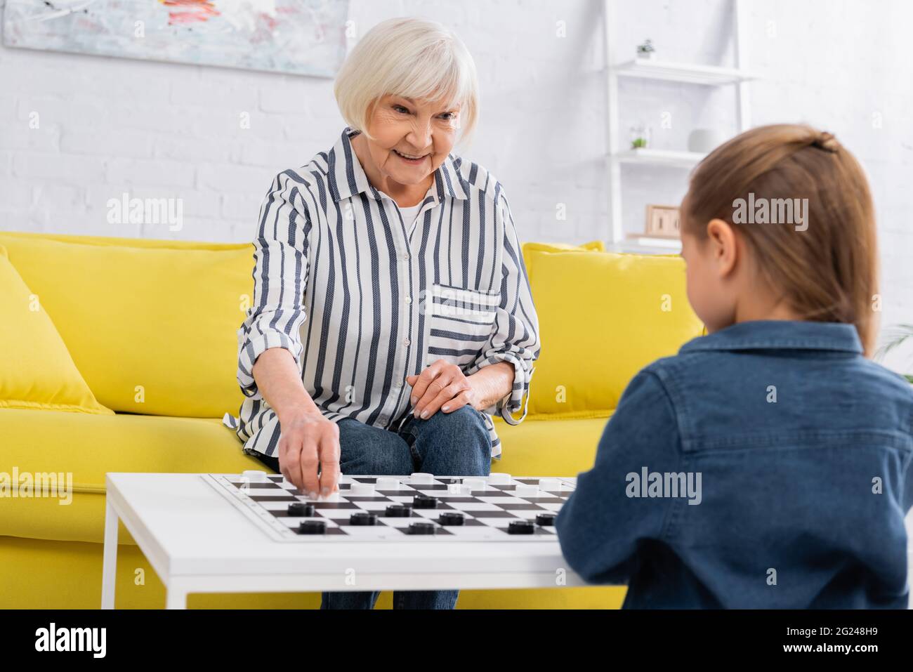 Ältere Frau lächelt, während sie Dame mit verschwommenem Kind spielt Stockfoto