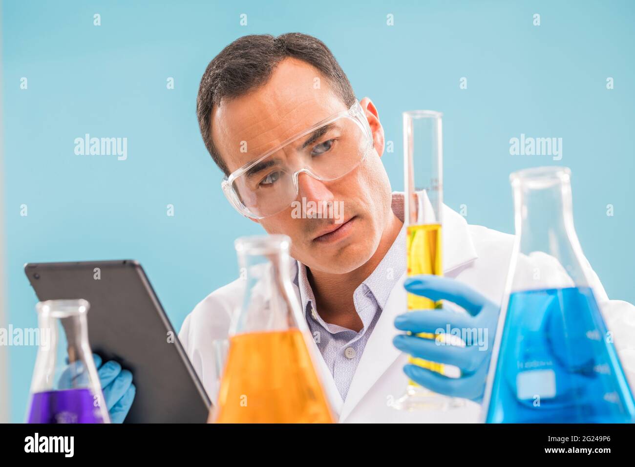 Wissenschaftler mit einem digitalen Tablet, das gelbe Flüssigkeit im Becher betrachtet Stockfoto