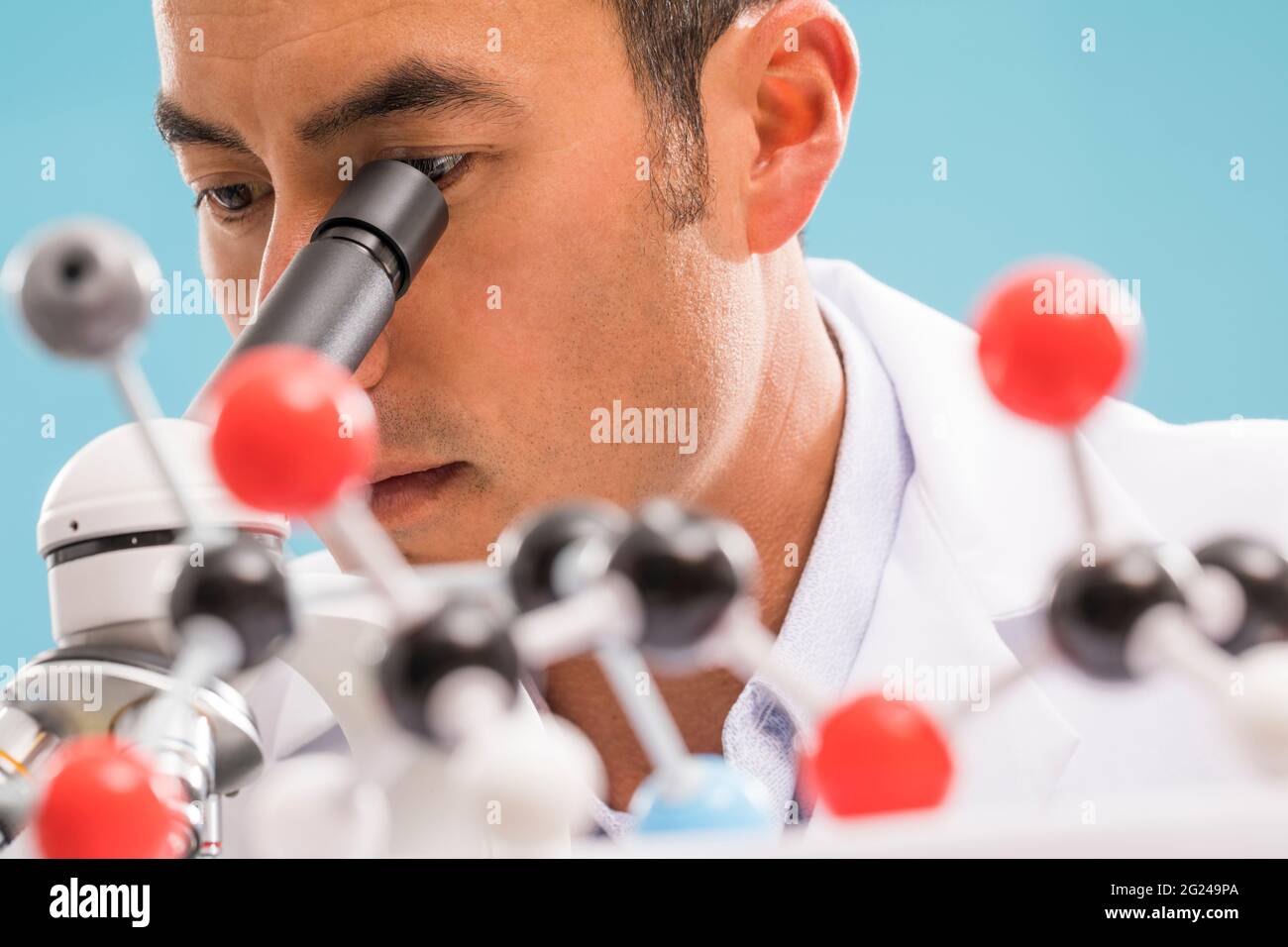 Nahaufnahme eines Wissenschaftlers, der durch das Mikroskop schaut, molekulares Modell im Vordergrund Stockfoto