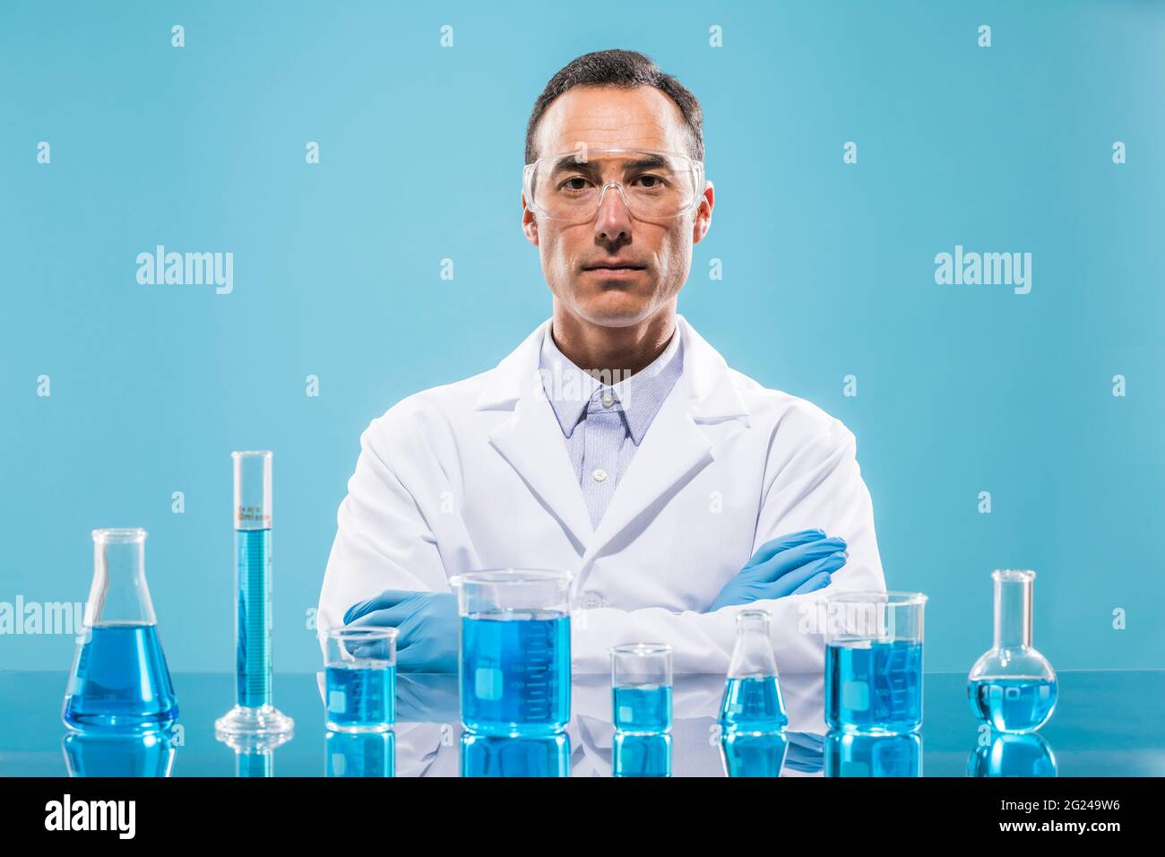 Porträt eines Wissenschaftlers mit Bechergläsern mit blauer Flüssigkeit im Vordergrund Stockfoto